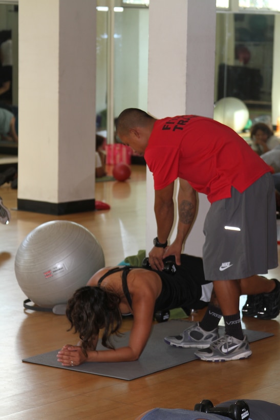 Gene Calantoc, personal trainer, puts a weight on Chief Petty Officer La Dala's back while she does a plank during an abs class at the Semper Fit Center aboard Marine Corps Recruit Depot San Diego. Dala, who works at Naval Base San Diego, attends some of the abs classes held Monday through Thursday.  Calantoc leads participants through a variety of abdominal exercises using different equipment and targeting different core muscles.