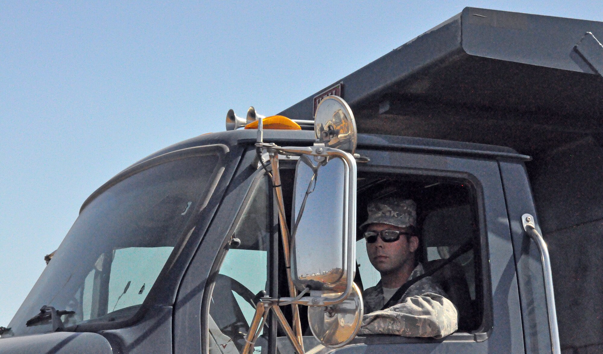 The driver of the dump truck waits for the log to be successfully placed in the vehicle before he drives through a desgnated trail backward, with points deducted for each cone knocked over. (U.S. Air Force photo/ Airman Madelyn Ottem)
