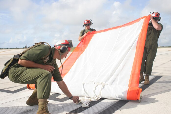 Lance Cpl. Pawel Jamiolkowski, a Marine Fighter Attack Squadron 115 aviation ordnance technician, Gunnery Sgt. Jason A. Hewes, VMFA-115 ordnance chief, and Cpl. Trevor J. Fortin, a VMFA-115 aviation ordnance technician, unravel a banner in preparation of an aerial banner shoot at the flight line here Oct. 10. The purpose of the shoot was to test Strike Fighter Squadron 94 and VMFA- 115 F/A-18 pilots in their aerial weapon proficiency with the M61A1 20mm Vulcan cannon.