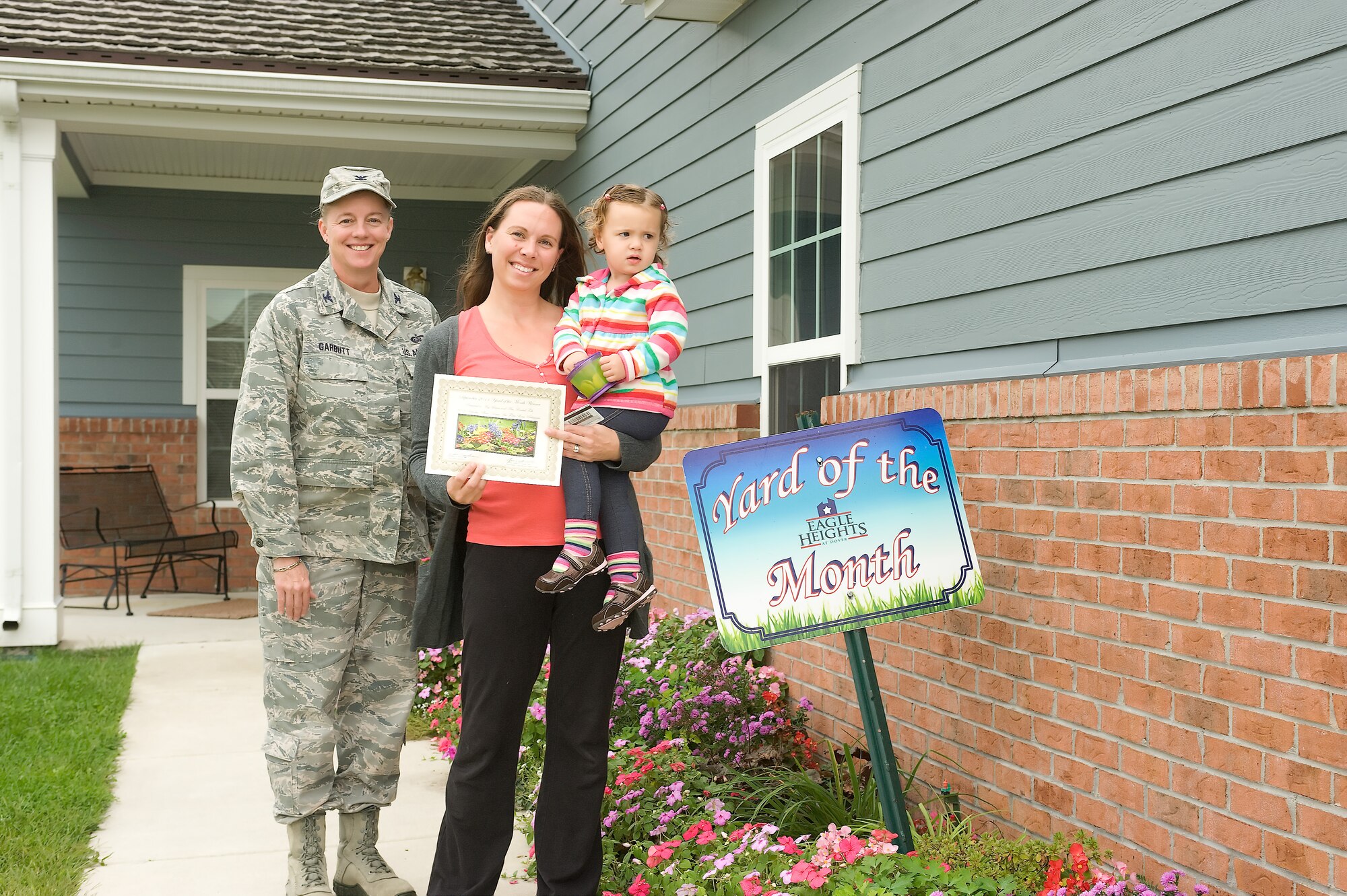 Col. Joan Garbutt (left), commander of the 436th Mission Support Group, stands with Rachel Toth, wife of Maj. Brent Toth, and their daughter Elise, recognizing the Toth family as the Falcon View Yard of the Month winner for September at Dover Air Force Base, Del. (U.S. Air Force photo by Steve Kotecki)