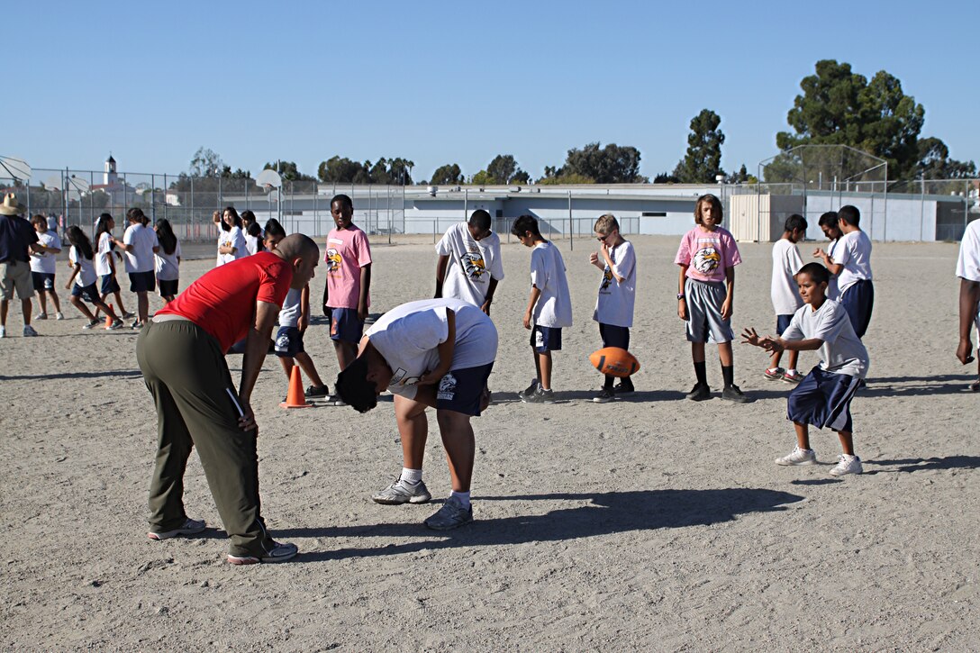 Staff Sgt. Jarvis Rodriguez, a drill instructor with 1st Recruit Training Battalion, Alpha Company, works with two students on how to snap the ball during a visit to Taft Middle School as part of the Partnership in Education Program Tuesday. The PIE program consists of Marine volunteers visiting the school every other Tuesday to participate in physical educations classes in an effort to provide the students with positive role models.