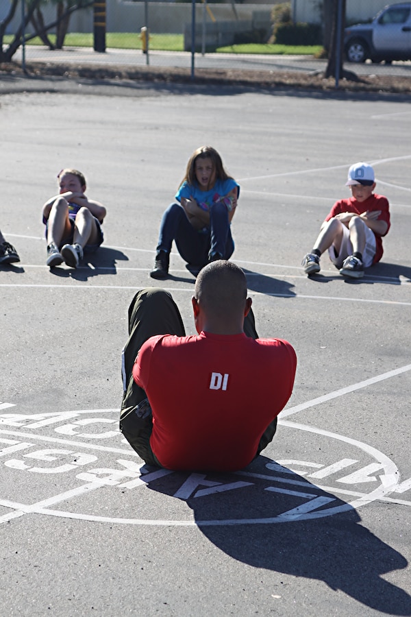 Staff Sgt. Owein M. Ramirez, a drill instructor with 1st Recruit Training Battalion, Alpha Company, does crunches with students during a visit to Holmes Elementary School as part of the Partnership in Education Program Tuesday. The PIE program consists of Marine volunteers visiting the school every other Tuesday to participate in physical educations classes in an effort to provide the students with positive role models.