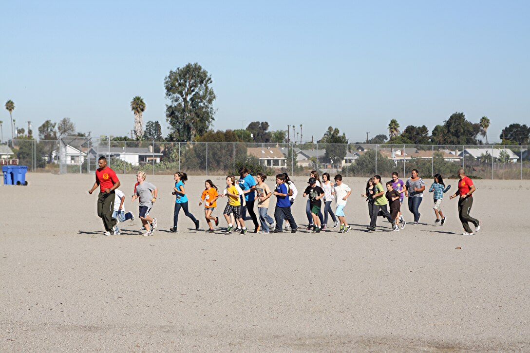 Staff Sgt. Owein M. Ramirez and Staff Sgt. Jarvis Rodriguez, drill instructors with 1st Recruit Training Battalion, Alpha Company, run with students during a visit to Holmes Elementary School as part of the Partnership in Education Program Tuesday. The PIE program consists of Marine volunteers visiting the school every other Tuesday to participate in physical educations classes in an effort to provide the students with positive role models.