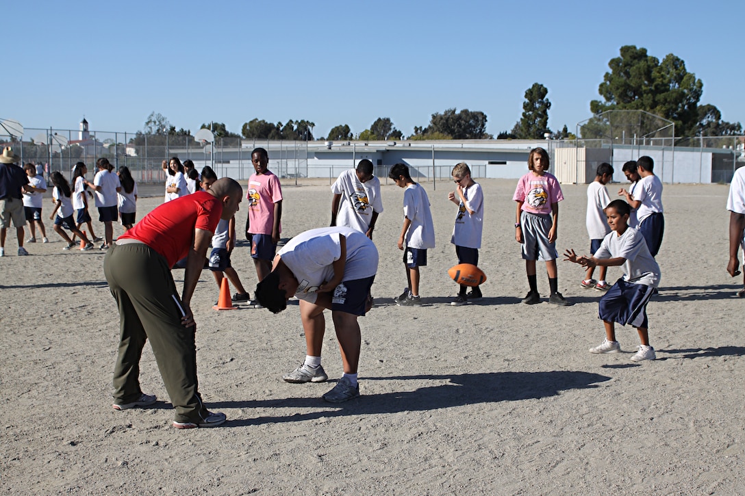 Staff Sgt. Jarvis Rodriguez, a drill instructor with 1st Recruit Training Battalion, Alpha Company, works with two students on how to snap the ball during a visit to Taft Middle School as part of the Partnership in Education Program Tuesday. The PIE program consists of Marine volunteers visiting the school every other Tuesday to participate in physical educations classes in an effort to provide the students with positive role models.