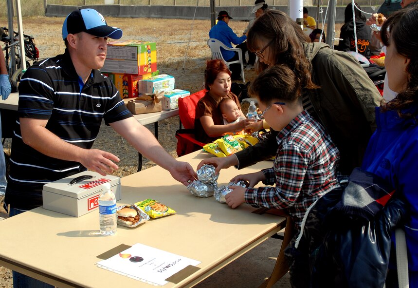 Tech. Sgt. Roger Deshaies, 8th Maintenance Squadron Magnum senior quality assurance evaluator, hands a Korean family pulled pork sandwiches during the 2011 Gunsan-Saemangeum Air Show at Kunsan Air Base, Republic of Korea, Oct. 8, 2011. The air show featured many static displays and performances from across the Pacific Air Forces and Korean peninsula. (U.S. Air Force photo by Senior Airman Benjamin Stratton/Released)