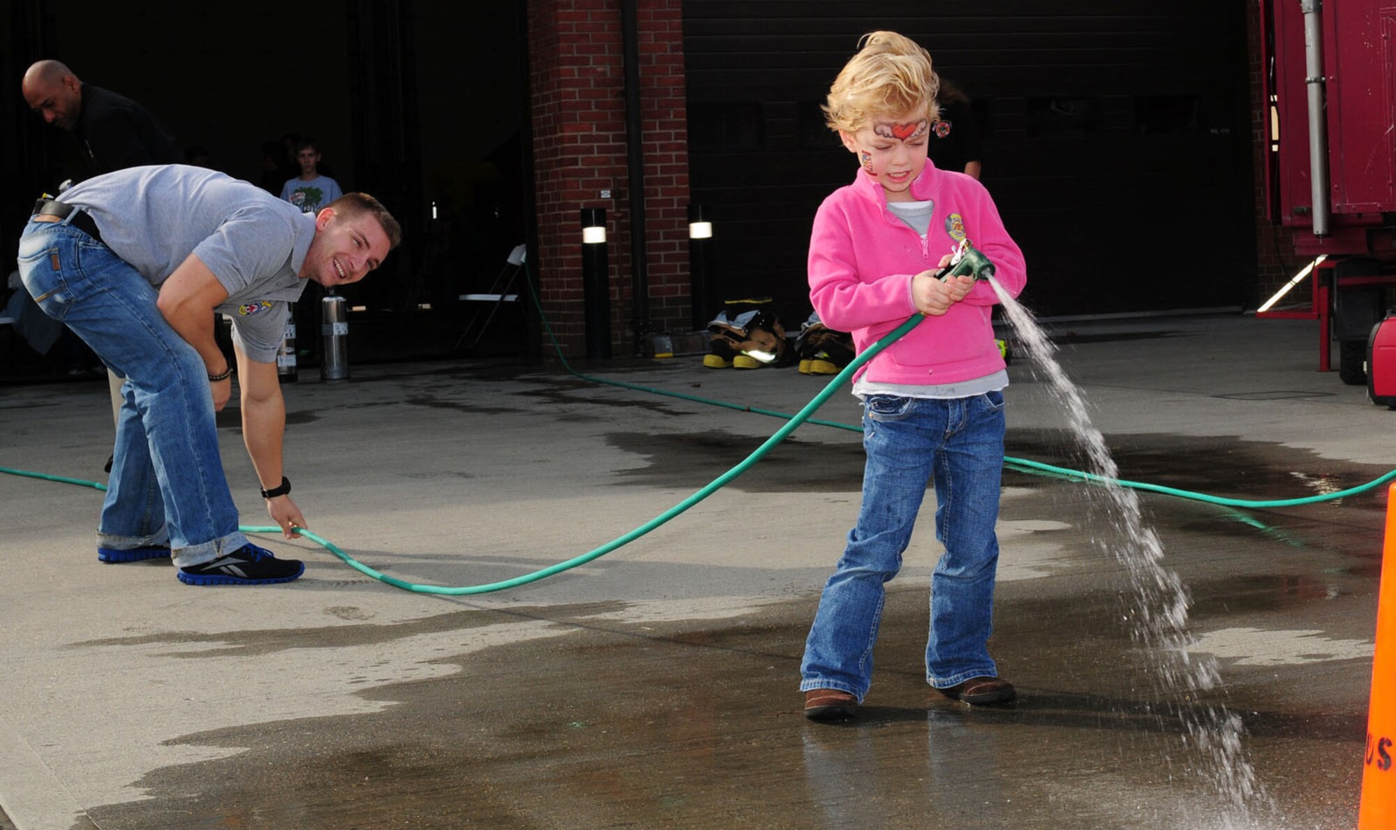 RAF MILDENHALL, England -- Staff Sgt. Noah Leiter, 100th Civil Engineer Squadron Fire Department, helps Taylor Frederickson, 5, daughter of Tech. Sgt. Carrie Frederickson, 48th Civil Engineer Squadron, as she sprays a garden hose during the children's fire muster here Oct. 10, 2011, at the RAF Mildenhall Fire Department's open house event. The open house was just one the many Fire Prevention Week events, which also included Firefighter Gary and friends at the food court, a visit to RAF Lakenheath's youth center and a fire muster. (U.S. Air Force photo by Karen Abeyasekere)