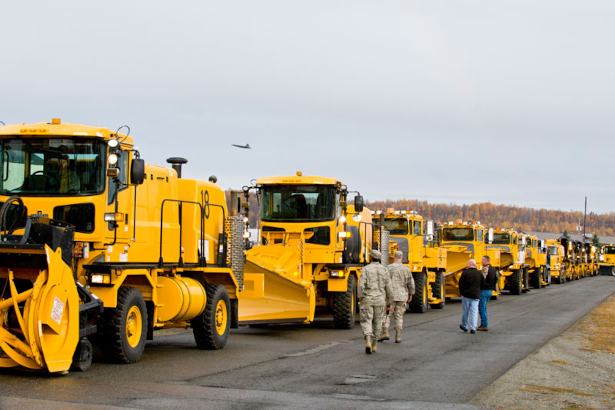 JOINT BASE ELMENDORF-RICHARDSON, Alaska -- Members of the 773rd Civil Engineer Squadron walk down the line of snow removal machines, just as an F-22 takes off, for inspection just prior to the beginning of the parade on JBER, Oct. 7. The 773rd CES's equipment was preparing for its annual parade to display the equipment used to remove snow on base. (U.S. Air Force photo/Johnathon Green)