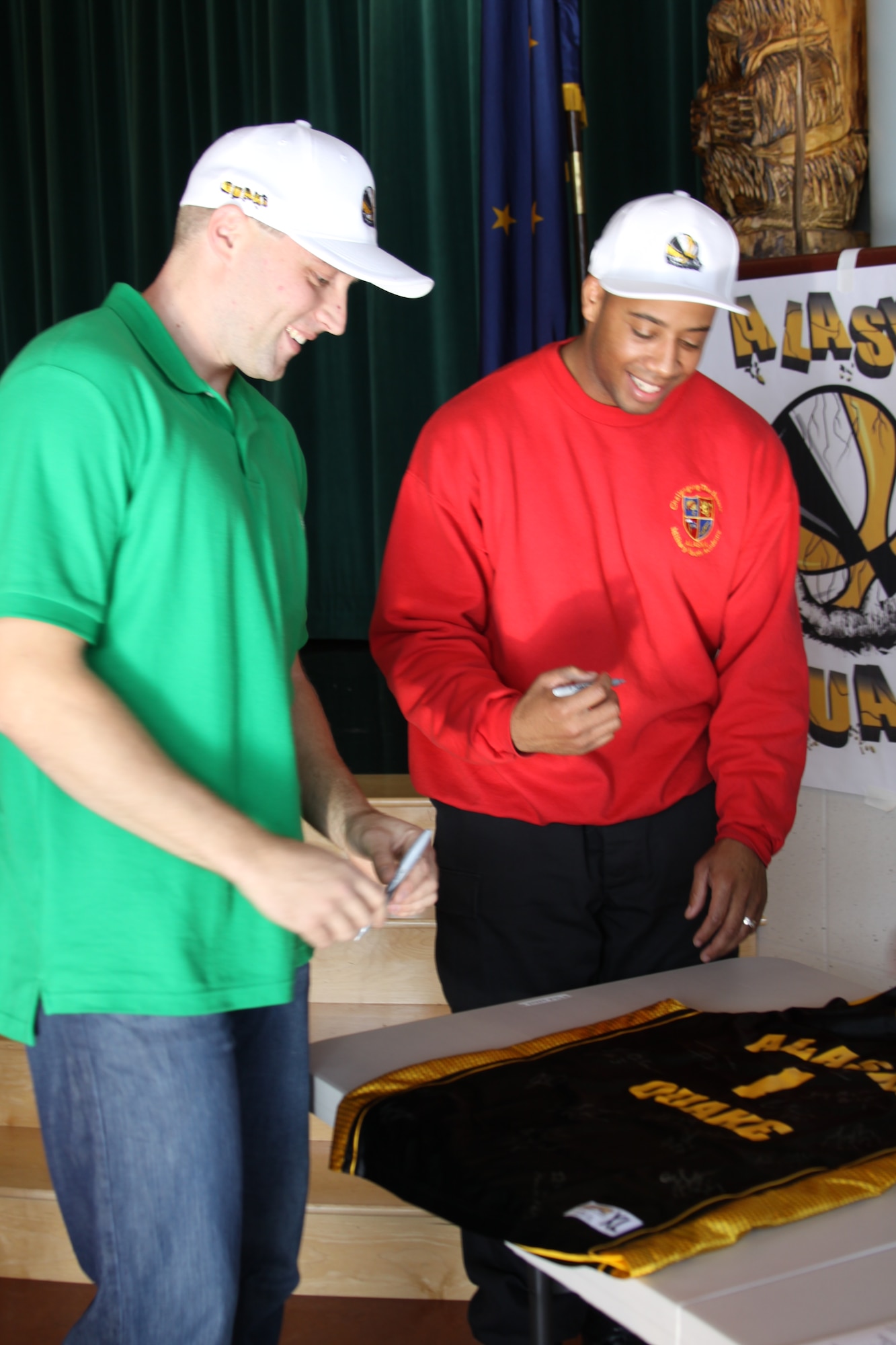 Master Sgt. Jonathon Orzechowski, an Air Force Reservist with the 477th Civil Engineer Squadron and SGT Joey Lewis with the Army National Guard’s E Company, 1-207th Aviation, the newest members of the Alaska Quake basketball team sign a jersey during the team’s meet and greet at Begich Middle School Oct. 8 (U.S. Air Force Photo/ Capt. Ashley Conner) 