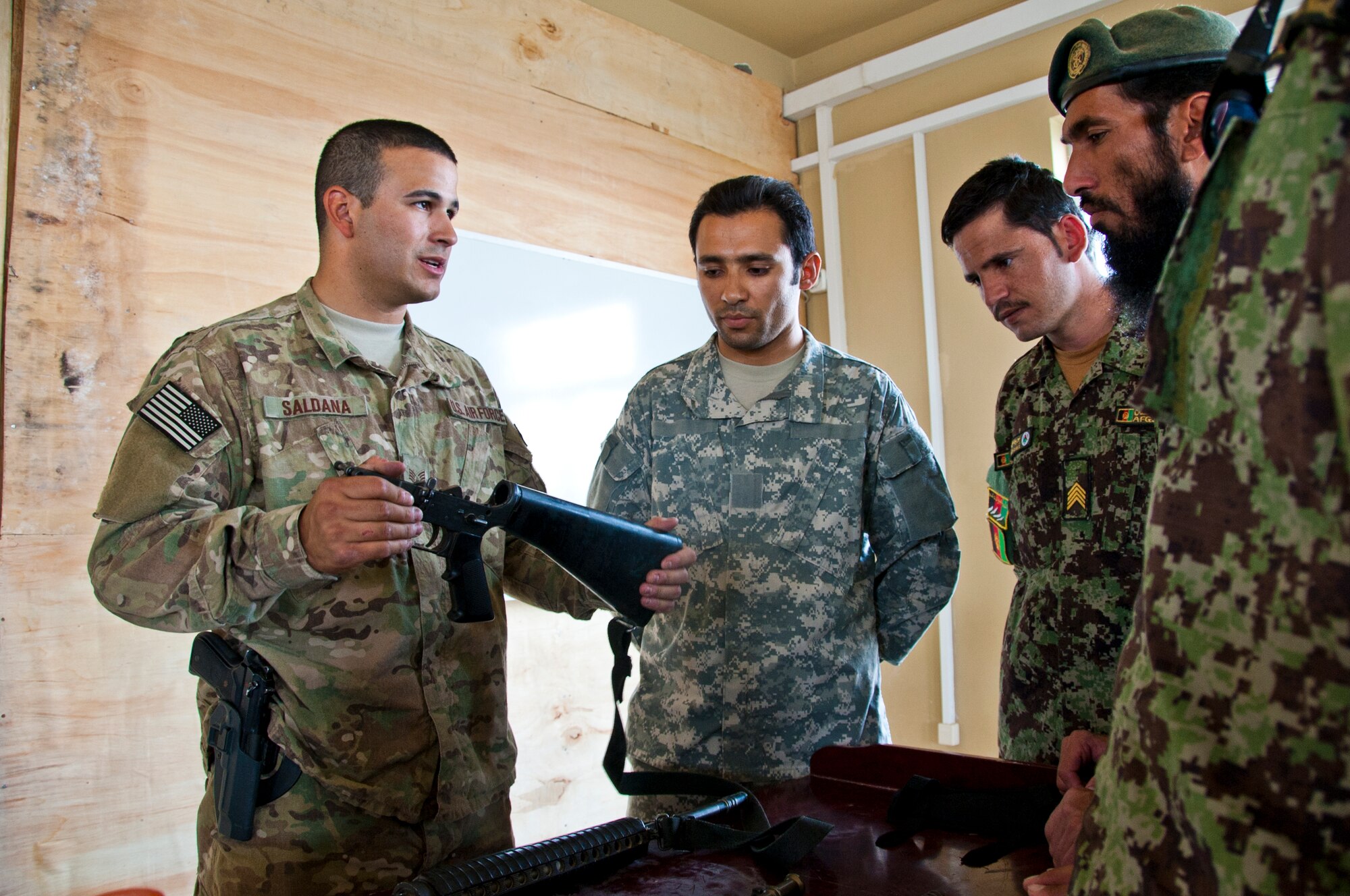 KANDAHAR AIRFIELD, Afghanistan -- Staff Sgt. Mark Saldana, 451 Expeditionary Security Forces Squadron Combat Arms Training and Maintenance, talks about the lower assembly of an M-16 to members of the Afghan air force during a training session Oct. 13 at Kandahar Air Wing. For the past several weeks, the CATM team has been training the AAF on disassembly and troubleshooting issues on small arms. (U.S. Air Force photo by Senior Airman David Carbajal)