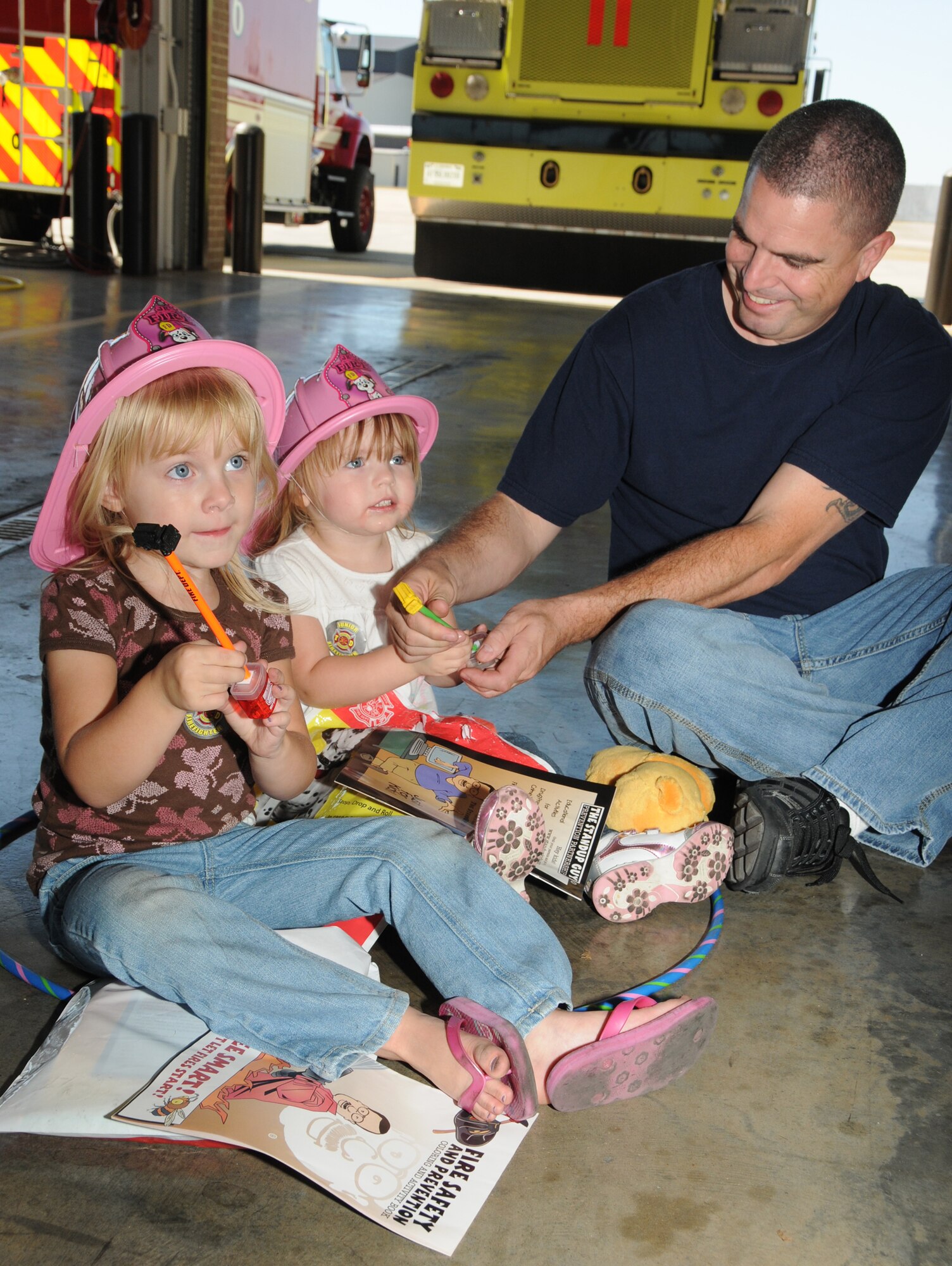 Left, Kylie Matthes, 4, Abagail Ouellet, 2, and their dad, Senior Chief  Petty Officer Dylan Ouellet, Center for Naval Aviation Technical Training Unit, Keesler Air Force Base, Miss., looks at the prizes they received in their goody bags during the Keesler Fire Department open house Oct. 15, 2011.  The event was the finale to Fire Prevention Week held Oct. 11-15, 2011.  (U.S. Air Force photo by Kemberly Groue)