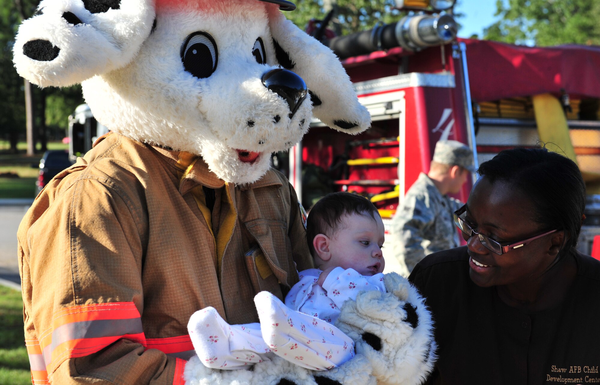 Sparky the Fire Dog holds Oliva Budzko while Brenda Petty, Child Development Center program assistant, tries to get her to smile at the Child Development Center at Shaw Air Force Base, S.C. Oct. 14, 2011. Sparky visited with children from the CDC in support of Fire Prevention Week. (U.S. Air Force photo by Airman 1st Class Amber E. N. Jacobs/Released)