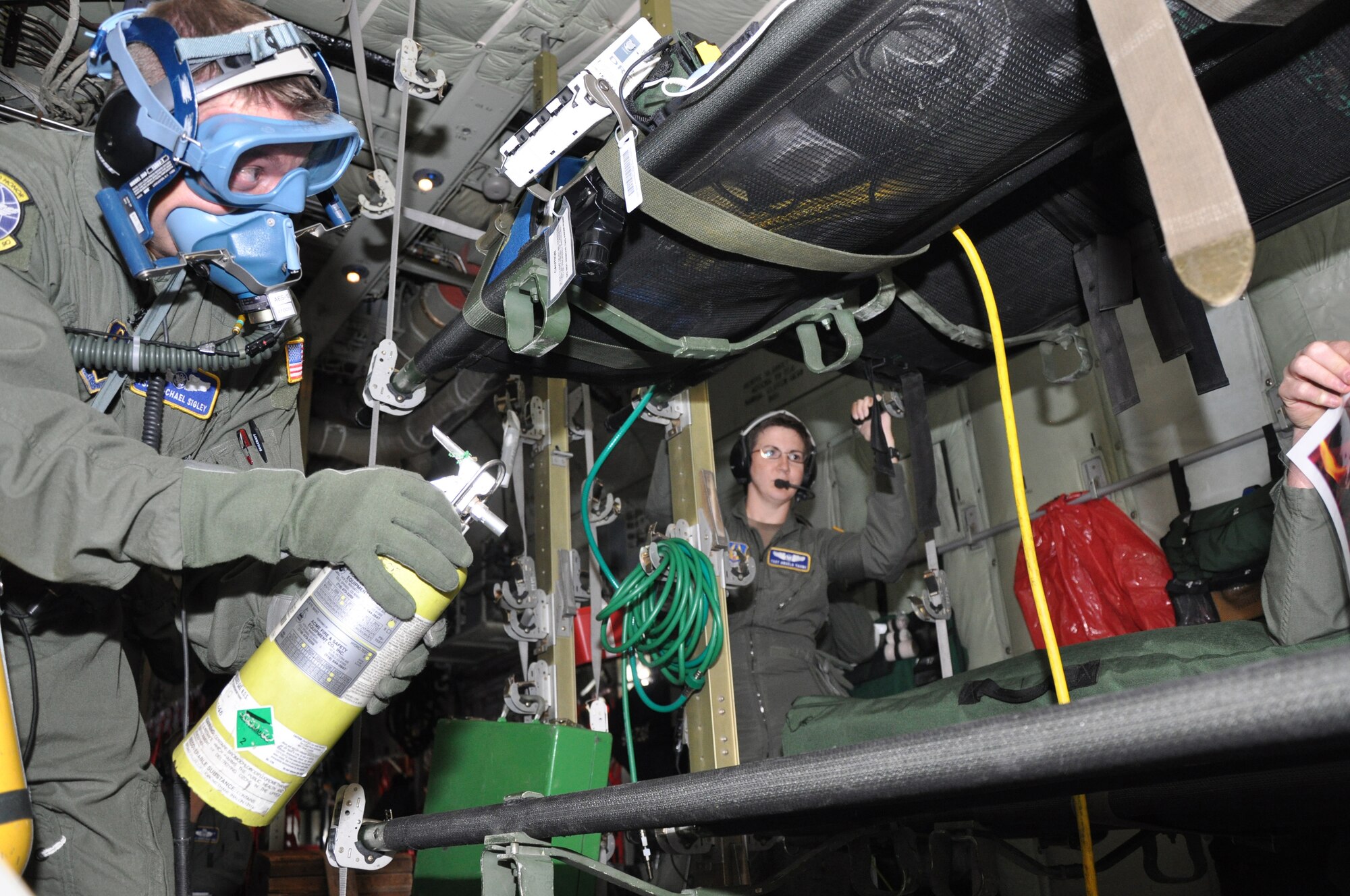 Tech. Sgt. Michael Sigley a 34th Aeromedical Evacuation Squadron technician simulates extinguishing a fire during an Oct. 3 AES training mission as evaluator, Tech. Sgt.  Angela Yahne, a flight instructor  instructor with the 34th AES looks on. The two took part in a routine aeromedical readiness training mission at Peterson Air Force Base, Colo. (U.S. Air Force photo/Tech. Sgt. Peter Dean)