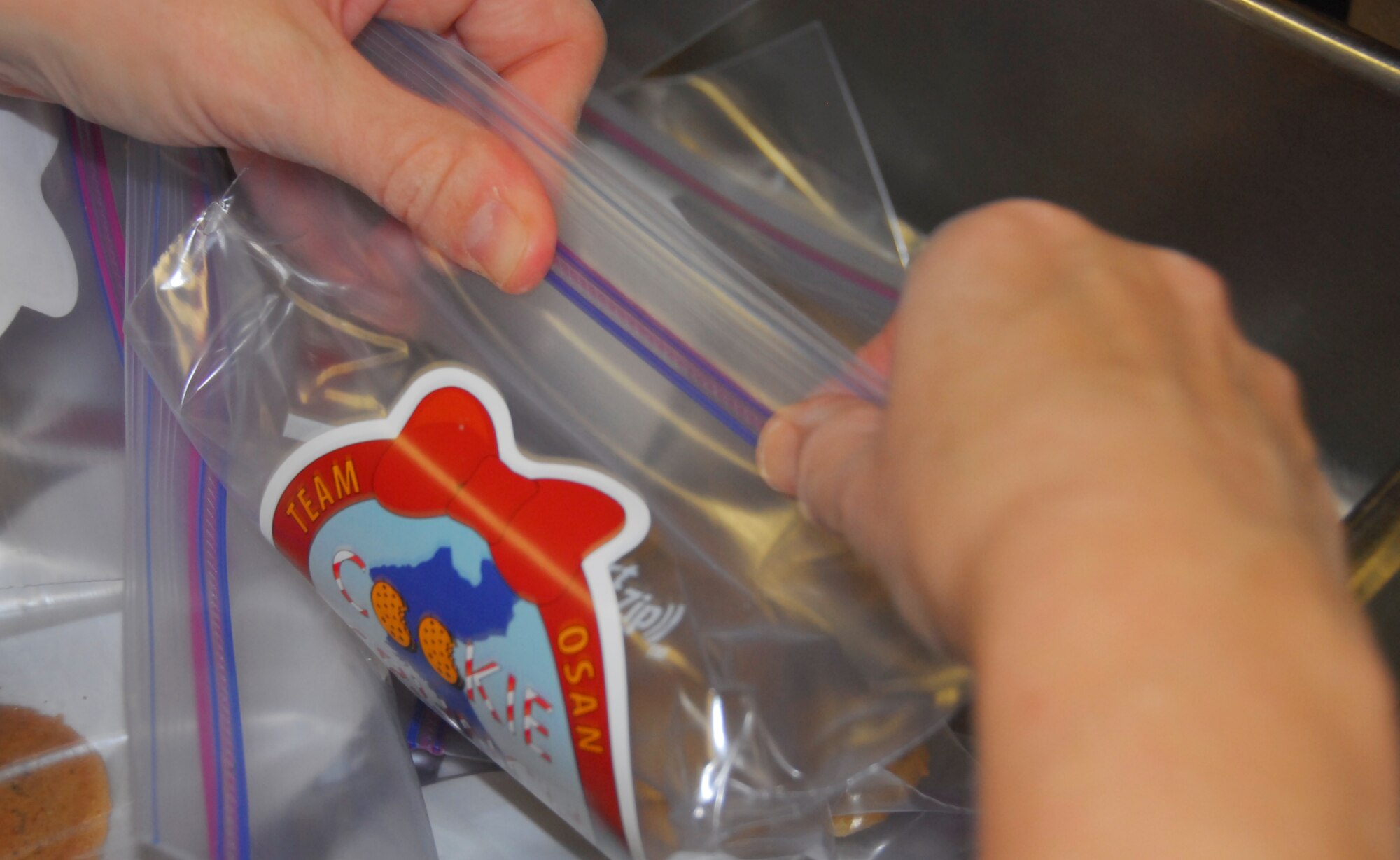 Zipping closed the plastic with eight cookies is the last station on the "Cookie Crunch" assembly line in the Mustang Club kitchen.  As of Oct. 20, 2011, more than 30,000 cookies were ready for delivery.  "Cookie Crunch" is a holiday cheer project of the Osan Air Base Officer Spouses Club.  (Air Force photo by Senior Master Sgt. Stuart Camp)
