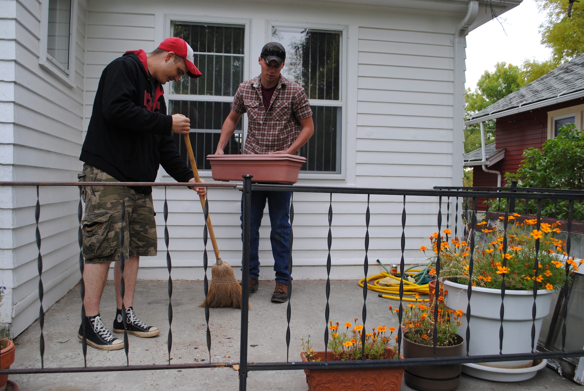 Airman 1st Class Brennden Baie, 741st Missile Security Forces Squadron security escort team guard, moves objects on a porch while Airman 1st Class Thomas Halley, also a 741st MSFS SET guard, sweeps under them.  Teamwork was one of the many qualities brought out in the members of Team Malmstrom that participated in the Day of Caring Oct. 14.  (U.S. Air Force photo/Airman Cortney Paxton)