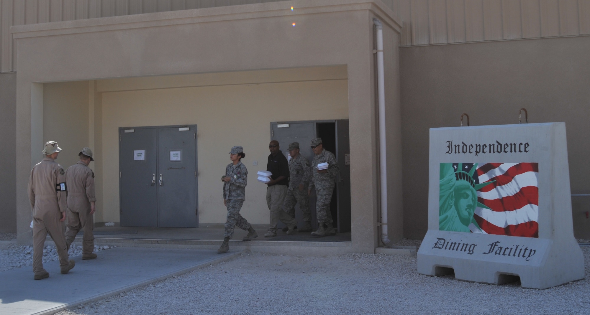 Airmen of the 379th Air Expeditionary Wing walk past a barrier painted by Tech. Sgt. Thomas Young and Staff Sgt. John Roys, in front of the Independence Dining Facility in Coalition Compound. Young and Roys are both part of the 379th Expeditionary Maintenance Squadron. (U.S. Air Force photo/Senior Airman Eric Summers Jr.)  