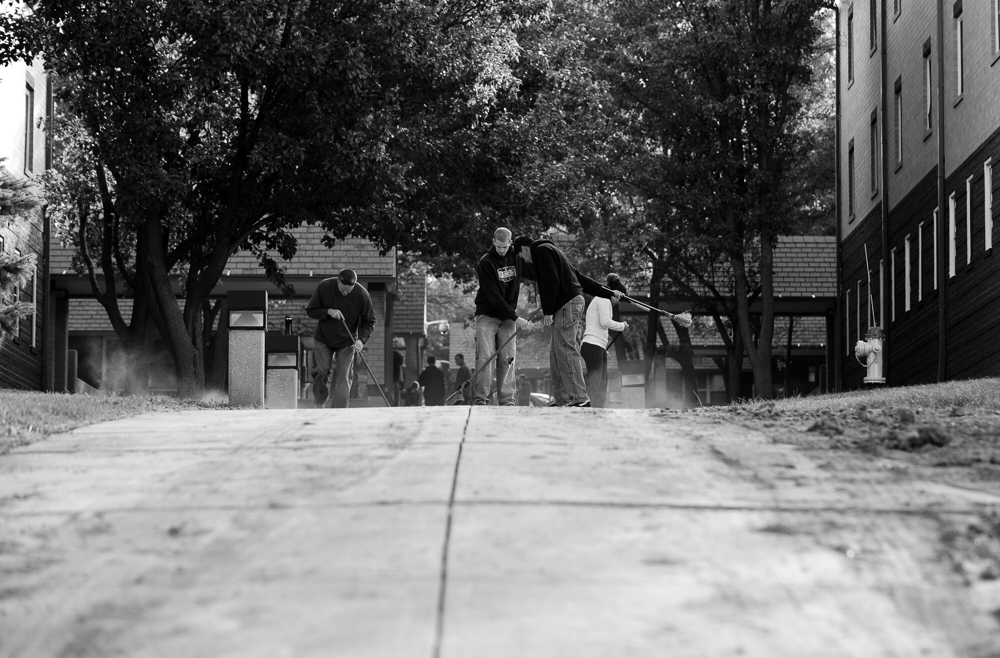 Clouds of dirt fill the air as the Airman clean the walkway between Kisling and Turner Hall during a dorm-wide clean-up held at Offutt Air Force Base, Neb., Sept. 24.  The shared efforts of dorm residents and Team Offutt volunteers resulted in a complete cleaning of the dorms. (U.S. Air Force photo by Josh Plueger/Released)