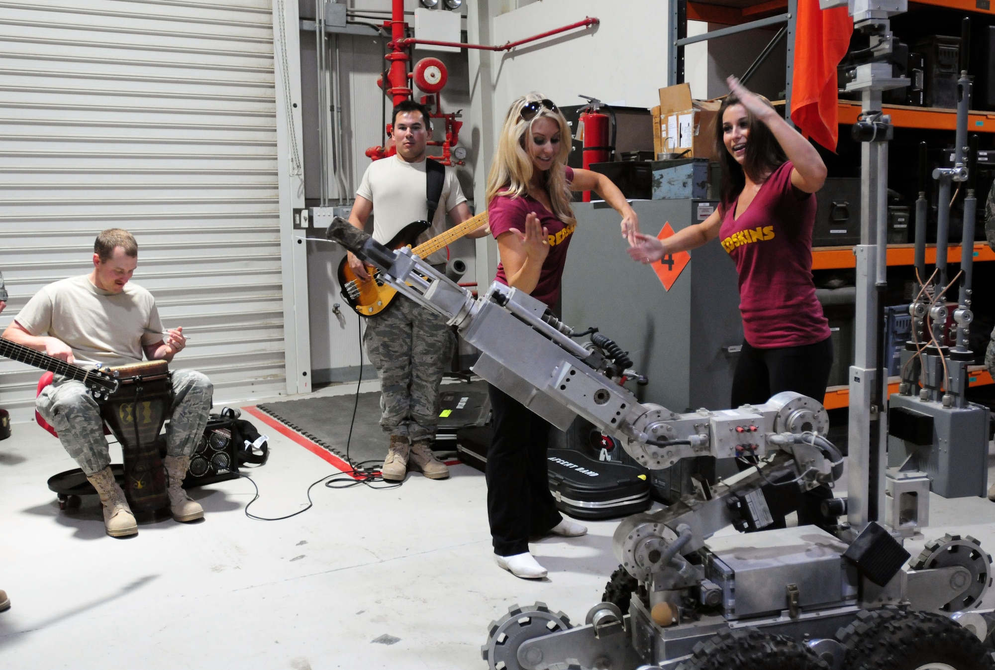 Washington Redskins Cheerleaders Amanda and Kristen dance with a robot from the Explosive Ordnance Disposal shop during a performance by Top Cover, the U.S. Air Forces Central Command band, at the 380th Air Expeditionary Wing in Southwest Asia Oct. 20, 2011. NFL players Marco Rivera and R.W. McQuarters and four members of the Washington Redskins Cheerleaders visited the 380th Air Expeditionary Wing Oct. 18-21 as part of the NFL Champions and the Washington Redskins Cheerleaders Tour from Armed Forces Entertainment. Top Cover also visited the base to perform for the deployed service members at the wing. Also pictured: Staff Sgt. Brandon Richard on drums and Airman First Class Philip Runge Jr. on bass. (U.S. Air Force photo/Capt. Gina Vaccaro McKeen)