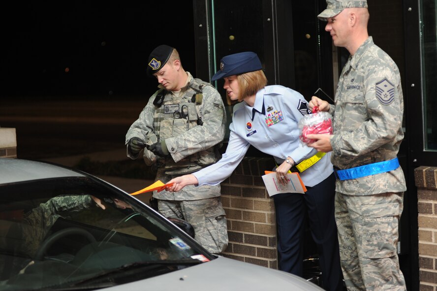 Airman 1st Class Luke Coffey, 22nd Security Forces Squadron member, checks identification cards at the front gate while Master Sgt. Heather Moody, 22nd Force Support Squadron Airman Leadership School commandant, along with Master Sgt.  Jeffrey Moody, 22nd Maintenance Operations Squadron first sergeant, hand out informational pamphlets about drug awareness and red ribbons Oct. 24, 2011, McConnell Air Force Base, Kan.  The event kicked off Red Ribbon Week, the nation’s oldest drug prevention program.  (U.S. Air Force photo/ Airman 1st Class Maurice Hodges)