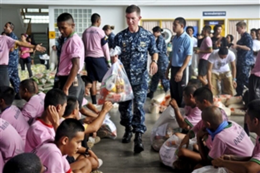 U.S. Navy Cmdr. Scott Tait hands members from the Thai navy a prepared packaged goods kit organized by the Princess Pa Foundation, Thai Red Cross Society, during a community service event, Oct. 23, 2011. Tait is commanding officer of the guided missile destroyer USS Mustin. More than 40 sailors from the Mustin assisted the local community and members of the Thai armed forces with preparing more than 5,000 packages.