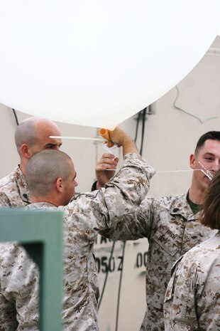 Sgt. Travis W. Patton and Staff Sgt. Michael E. Fitch, meteorology oceanography analyst forecasters, use zip ties in order to seal off the opening to a 300 gram weather balloon here Oct. 19. The Marines fill the balloon and hold it tight before attaching the Rawinsonde and release it so it may begin retrieving data.