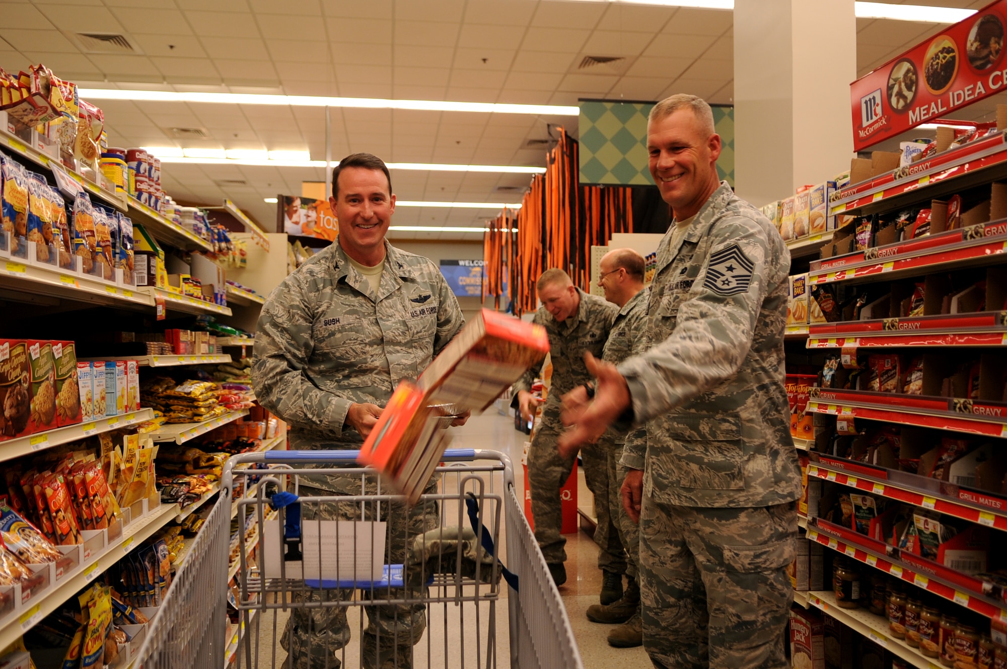 Col. Tim Bush, 319th Air Base Wing commander, left, and Command Chief Master Sgt. Dave Carlson, 319th Air Base Wing, toss items into a shopping cart to donate to Operation Warmheart at Grand Forks Air Force Base, N.D., on Oct. 25. The First Sergeant Council collects the donations to provide a no-cost Thanksgiving to Airmen on base. Donations are being accepted at the base commissary. (U.S. Air Force photo by Senior Airman Amanda N. Stencil)