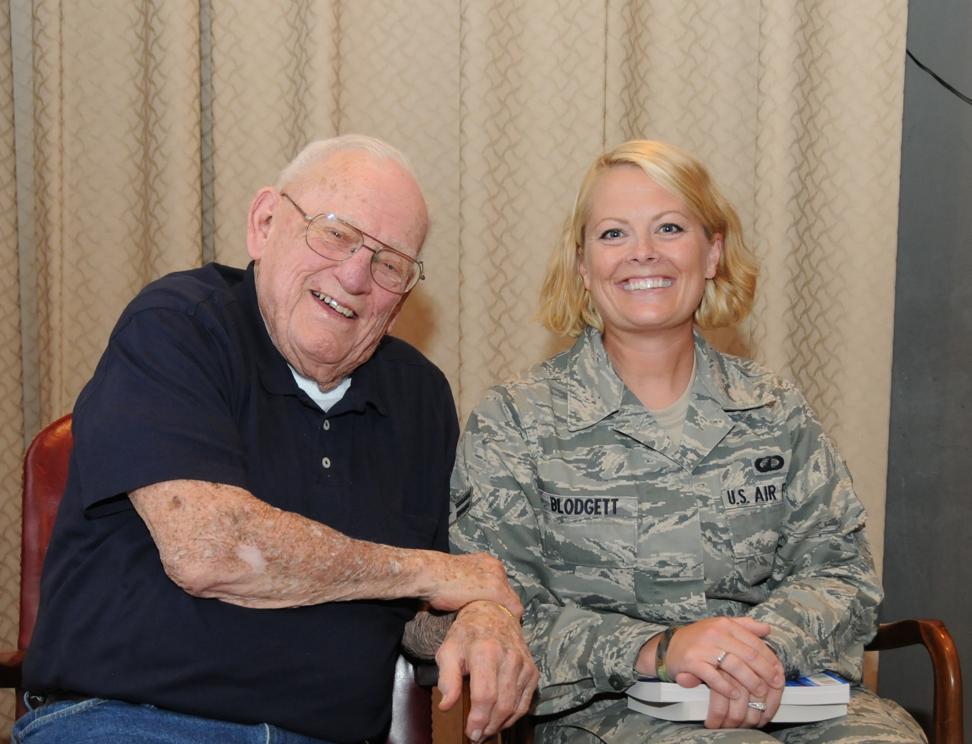 Airman 1st Class Amanda Blodgett, 173rd Fighter Wing Finance, has her picture taken with Lynn “Buck” Compton following the presentation August 32, 2011 at Kingsley Field, Klamath Falls, Ore.. She holds in her lap two books written by Compton and Malarkey respectively, recounting their experiences leading up to and during their days as Easy Company paratroopers. The two distinguished veterans happily signed books and took photographs with all who asked.