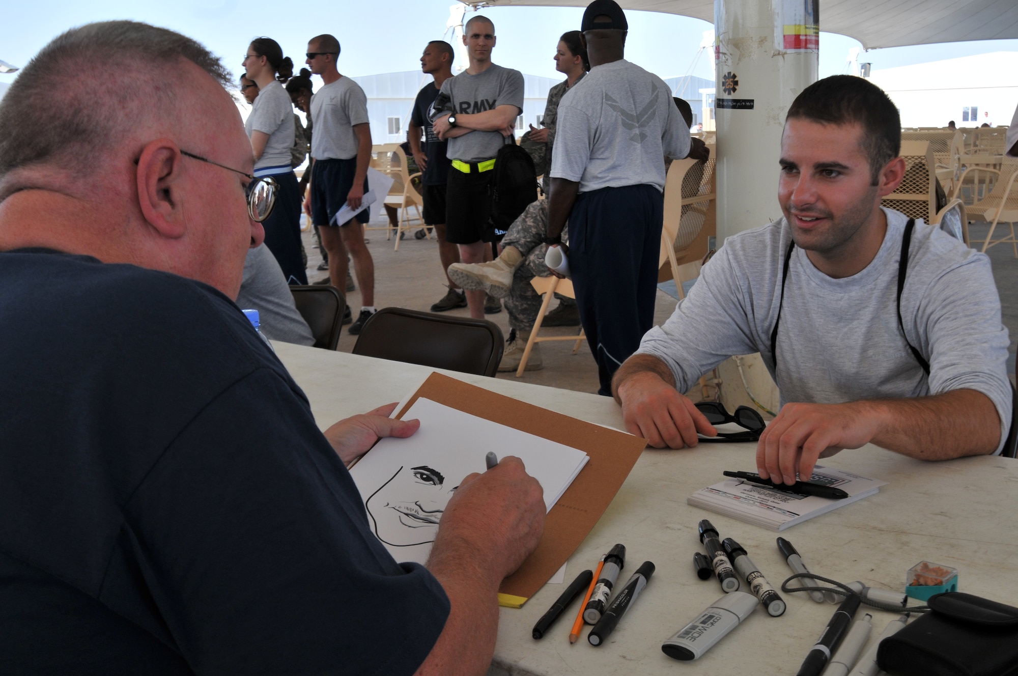 Senior Airman Joshua Mehdinia, 379th Expeditionary Civil Engineer Squadron firefighter, has a cartoon character of himself drawn by Bruce Higdon, Army cartoonist, during a USO-sponsored tour by National Cartoonists Society members Oct. 23, 2011, at an undisclosed location in Southwest Asia. The cartoonists visited several areas on base and drew pictures of servicemembers to help boost morale. Mehdinia, a native of Aurora, Colo., is deployed from Aviano Air Base, Italy. (U.S. Air Force photo/Senior Airman Eric Summers Jr.)
