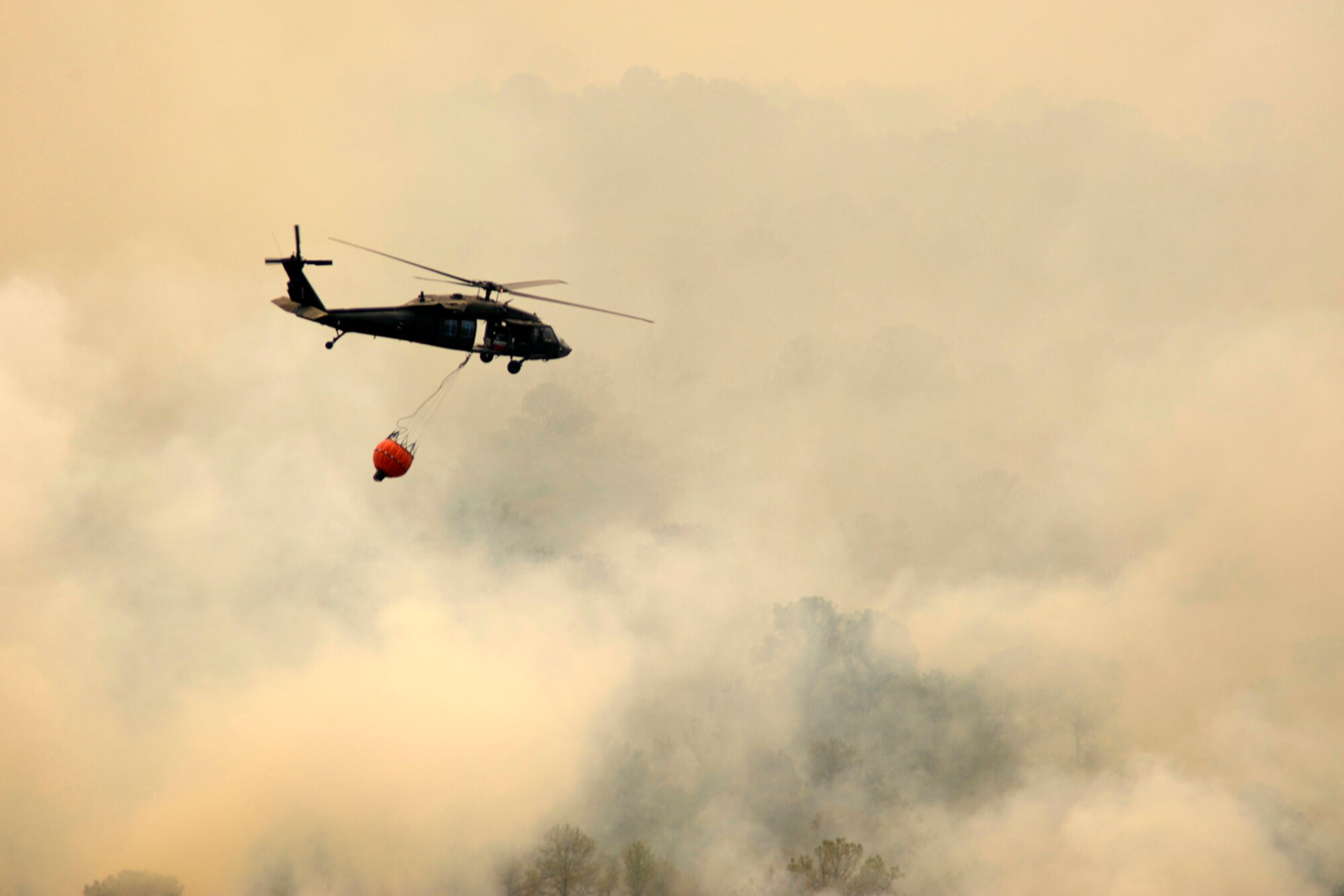 SPREADING LIKE WILDFIRE - A Texas National Guard CH-46 Blackhawk flies right into the smoke to dump its water over the wild fire. Texas National Guard crews launched out of the Austin Army Aviation Facility to fight wild fires threatening homes and property near Bastrop, Texas, September 6, 2011. (Photo by Staff Sgt. Malcolm McClendon)