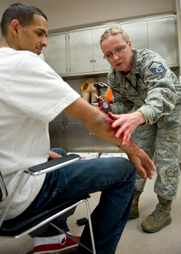 Master Sgt. Tricia Carnes, 28th Medical Support Squadron medical readiness and moulage team chief, creates the appearance of a minor burn on Senior Airman Rawlinson Fantaelon, 28th Maintenance Squadron crew chief, for a Chemical, Biological, Radiological, Nuclear and Explosives major accident response exercise at Ellsworth Air Force Base, S.D., Oct. 21, 2011. The wounded victims acted out their injuries to provide a realistic training scenario for medical personnel in order to better prepare them for a real world CBRNE attack. (U.S. Air Force photo by Airman 1st Class Kate Thornton/Released)
