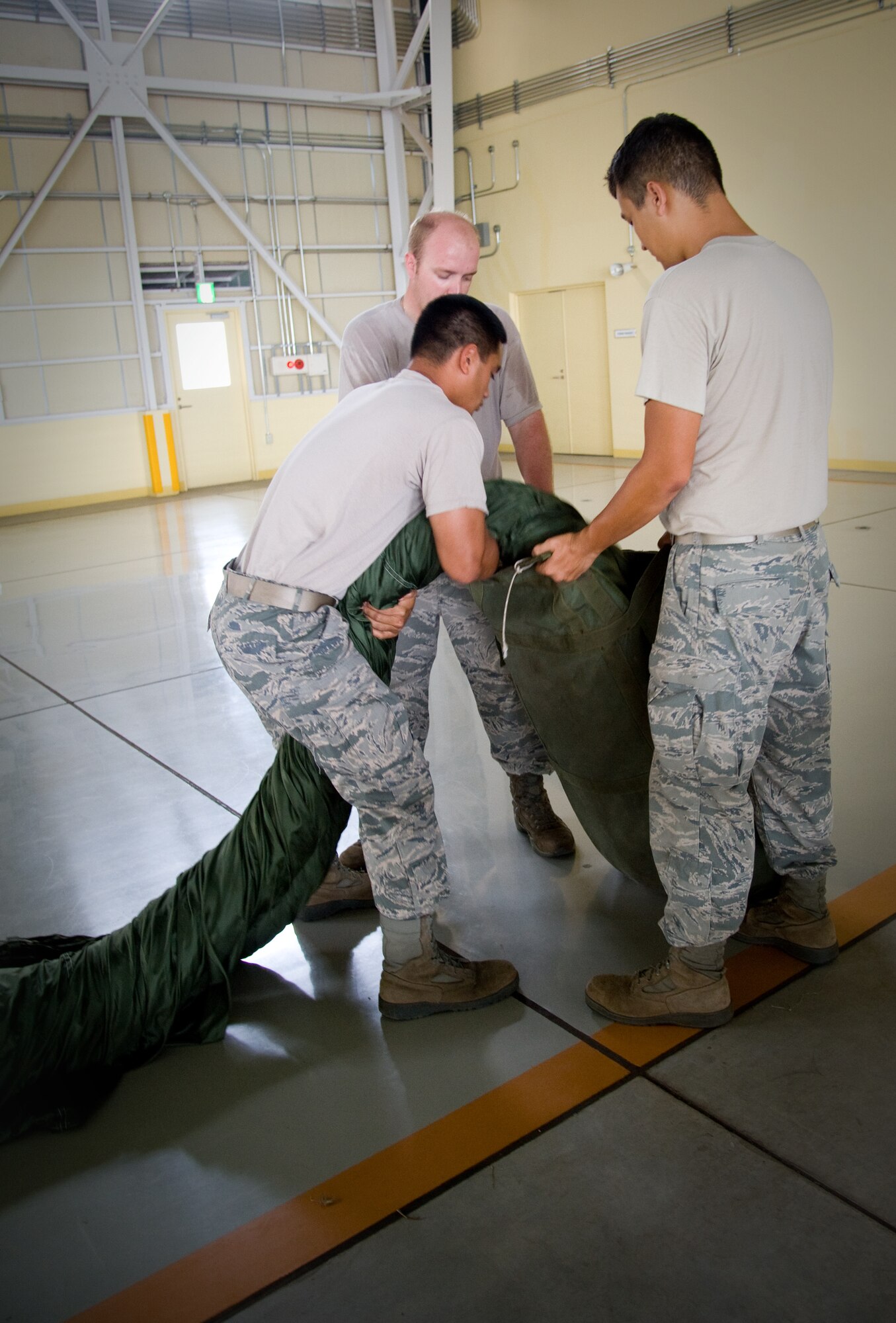 YOKOTA AIR BASE, Japan -- (Left), Airman 1st Class Marcus Ofoia-Stevens, (back), Senior Airman Brandon Wilson, (right), Airman 1st Class Adam Caton, 374th Logistics Readiness Squadron combat mobility flight riggers, pack a G-12 E parachute at Yokota Air Base, Japan, Sept. 1, 2011. G-12 E parachutes are used for heavy load airdrops. (U.S. Air Force photo/Airman 1st Class Krystal M. Garrett) 