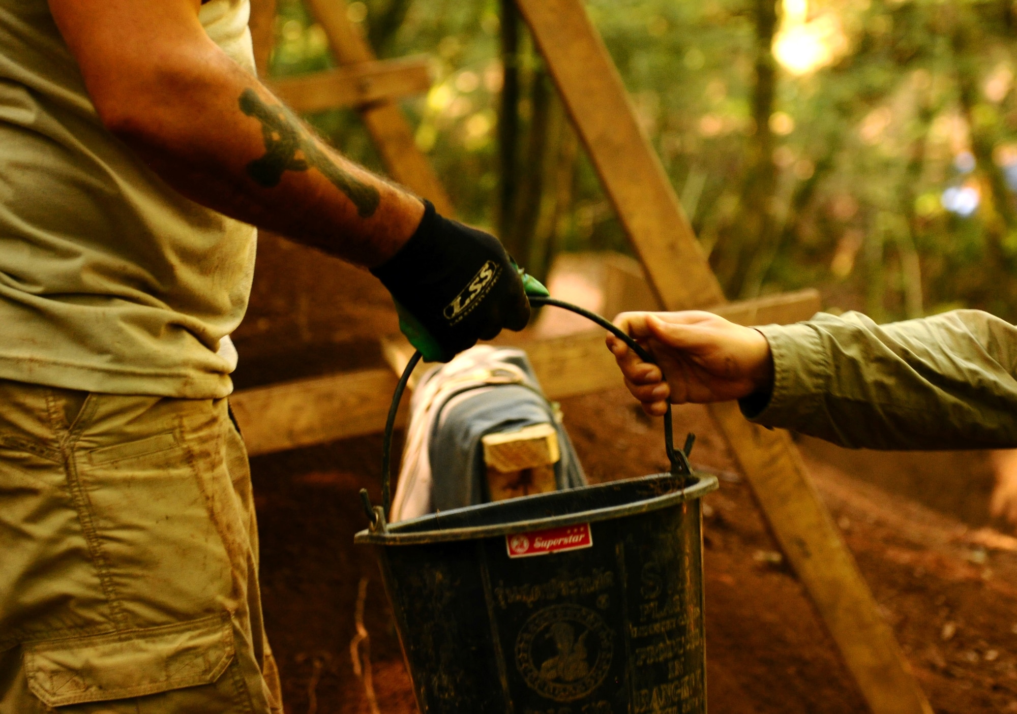 BETTENFELD, Germany -- U.S. Navy Mass Communications Specialist 1st Class Barry Hirayama, right, hands a bucket of dirt for sifting to U.S. Army Staff Sgt. Joe Meeks, both from the Joint POW/MIA Accounting Command, Honolulu, in search of the remains of two service members still unaccounted-for from World War II here Sept. 2. . Members of JPAC teamed up with U.S. volunteers from Spangdahlem Air Base to find the missing service members. The mission of JPAC is to achieve the fullest possible accounting of all Americans missing as a result of the nation's past conflicts. (U.S. Air Force photo/Staff Sgt. Nathanael Callon)