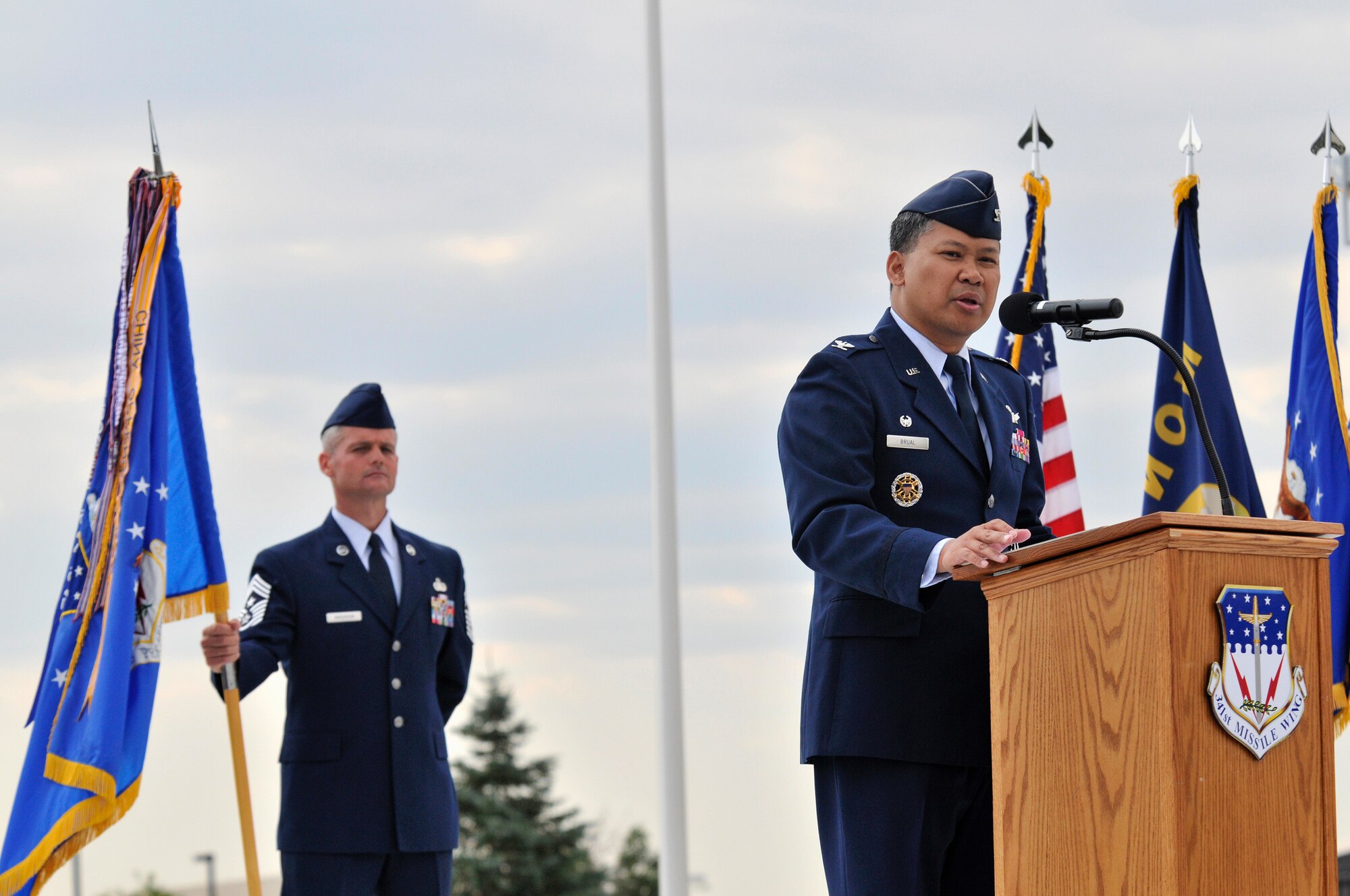 Col. Heraldo B. Brual speaks to the members of Wing One during his assumption of command ceremony Aug. 29 at Medal of Honor Park. Chief Master Sgt. Charles Anderson, 341st Missile Wing command chief, looks on, holding the 341st MW guidon.