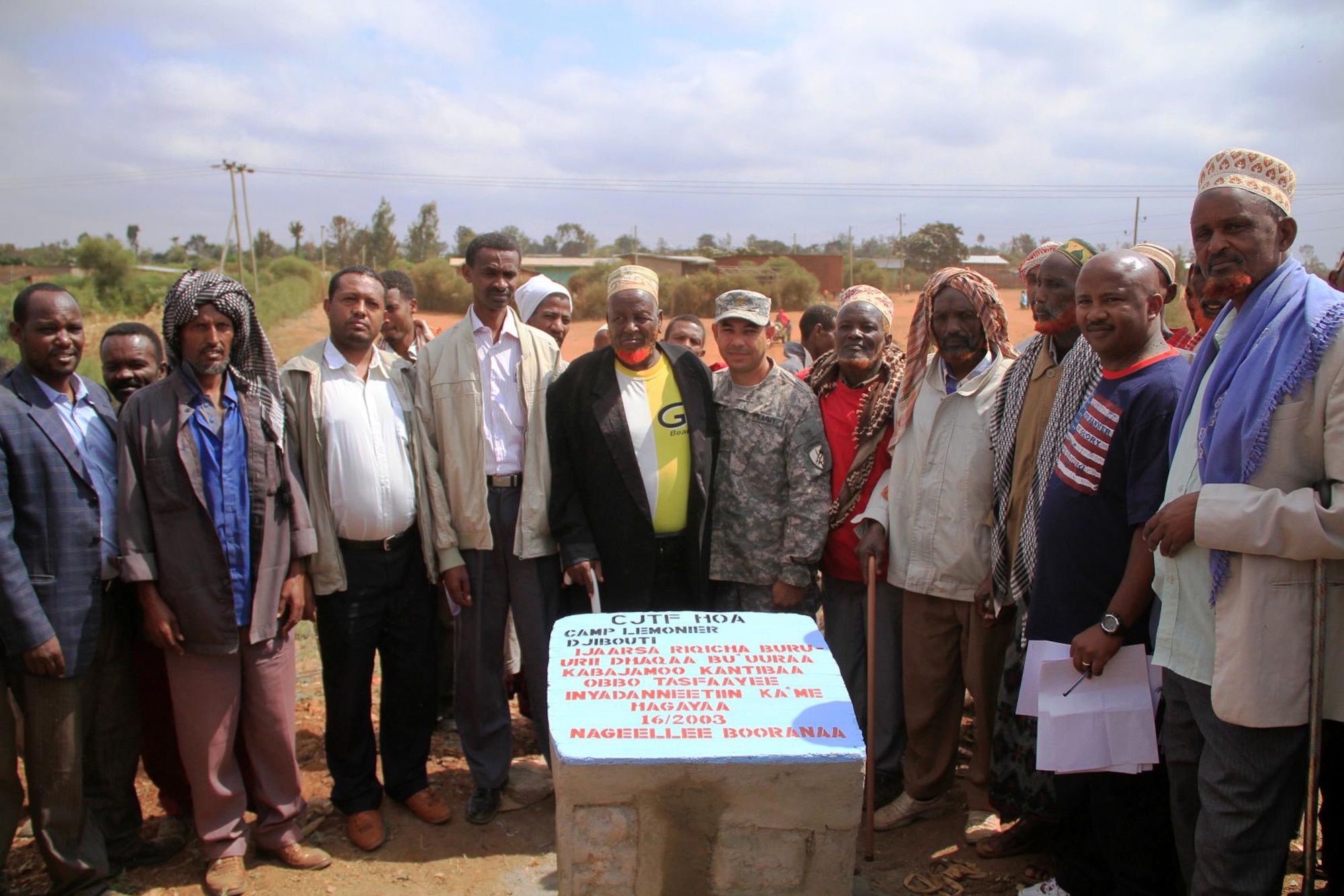 Village leaders, elders and bridge committee members gather around a stone marker to recognize the beginning of the bridge that will span a local river bed. The bridge will enable villagers on both sides safe access to the school, markets and medical facilities. (US Air Force Photo by Capt Jennifer Pearson)