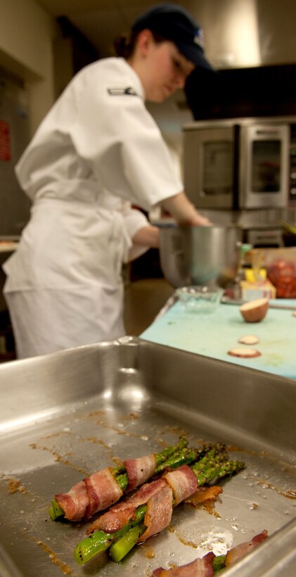 Bacon wrapped asparagus sets while Airman 1st Class Nichole Pierce, 28th Force Support Squadron food services apprentice, puts the finishing touches on a dessert during the Ellsworth Iron Chef competition at the Bandit Inn dining facility, Ellsworth Air Force Base, S.D., Aug. 26, 2011. Pierce’s team were runners up in the one-hour competition. (U.S. Air Force photo/Tech. Sgt. Jerry Fleshman/Released)