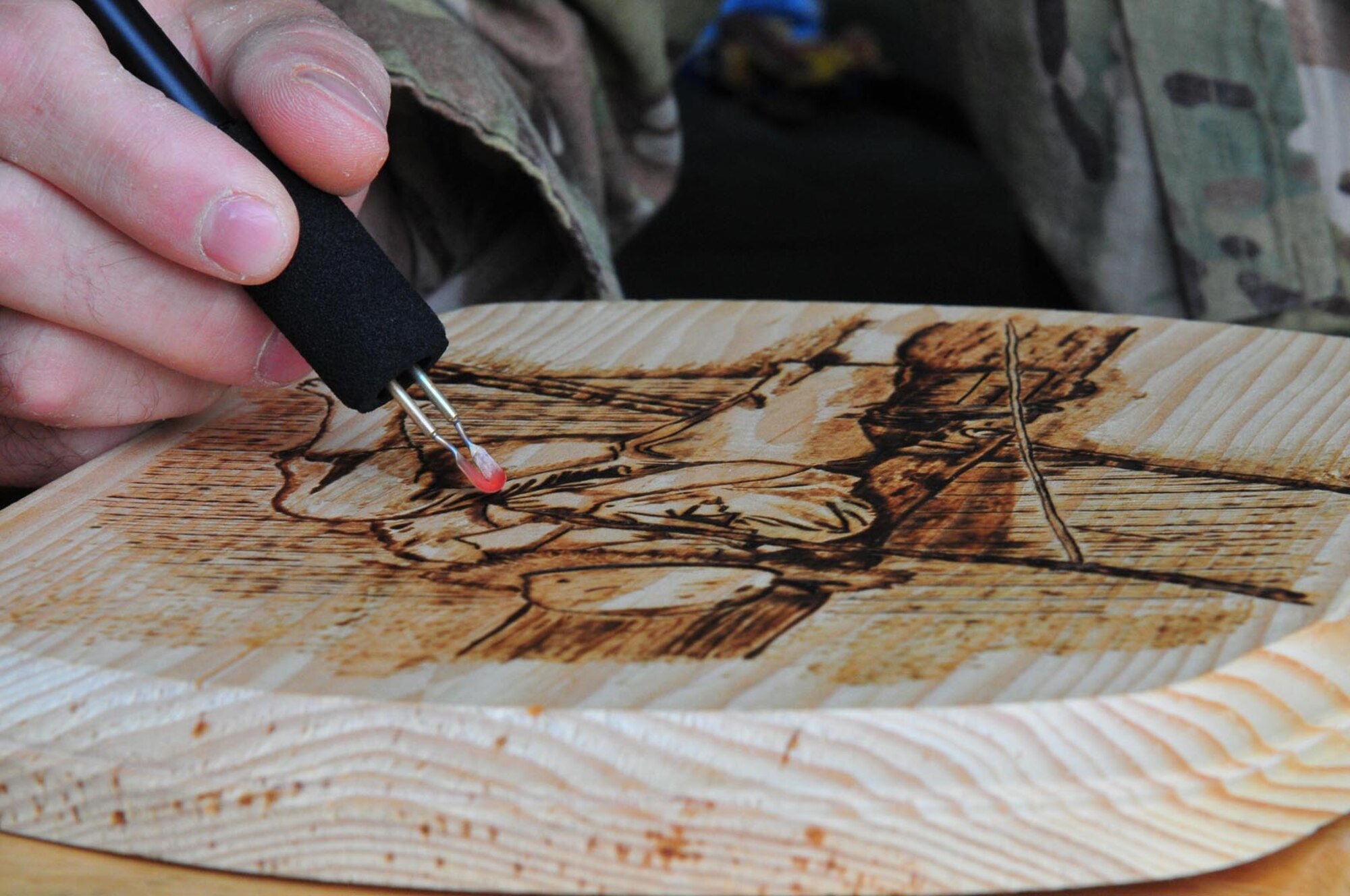 Using the tip of a hot wire tool, or nib, Staff Sgt. Omar Pagan, battle operations NCO with Task Force Resolute, 7th Sustainment Brigade, touches up his latest piece of pyrography, the art of burning marks into wood, Aug. 28 at Kandahar Airfield, Afghanistan. (US Army photo by Sgt. Edwin Rodriguez)