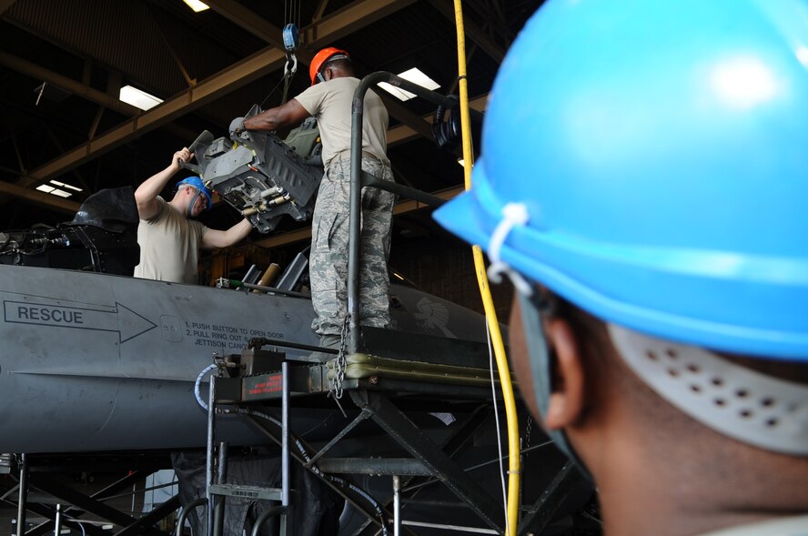 Staff Sgts. Richard Simmons and Stanley Houser guide an ACES II ejection seat onto an F-16 as Staff Sgt. Joseph Newton manipulates an overhead hoist in hanger 431 Sept. 6. Simmons, Houser and Newton are egress technicians with the 56th Component Maintenance Squadron. (U.S. Air Force photo by Senior Airman Tracie Forte)