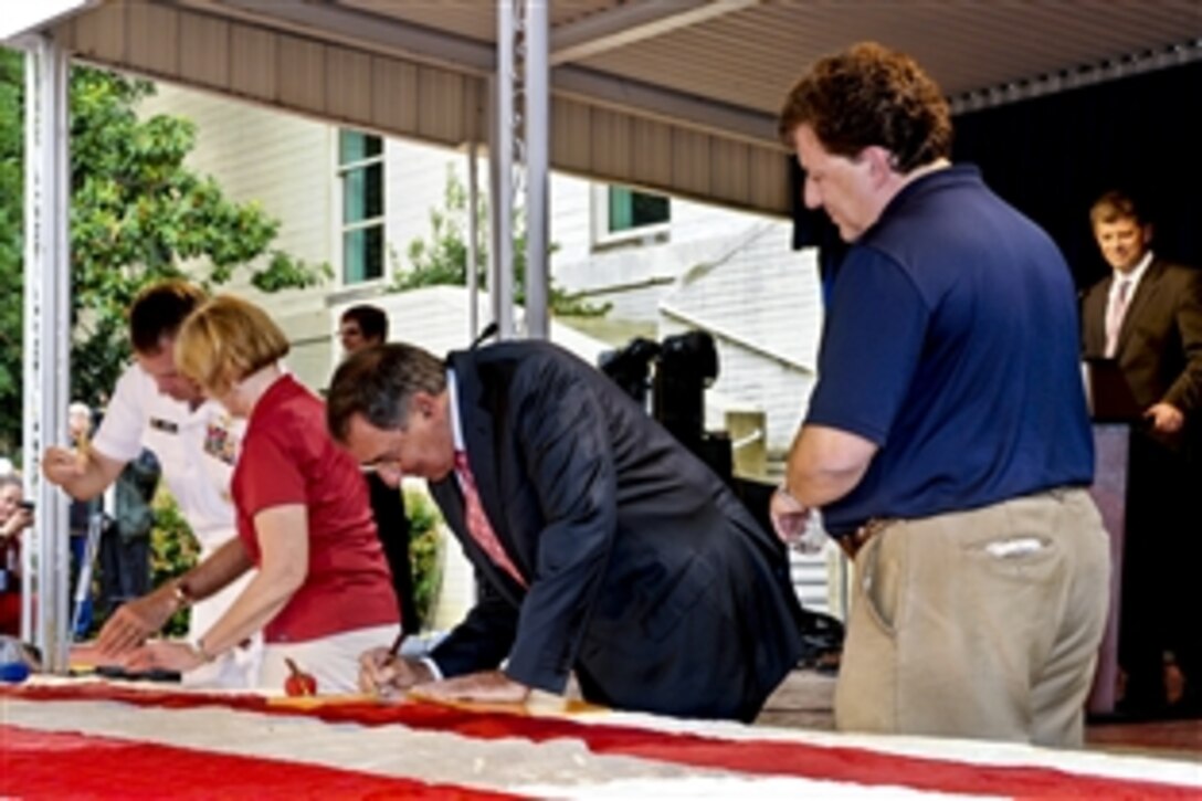 Defense Secretary Leon E. Panetta signs the guest book while Navy Adm. James A. Winnefeld Jr., left, vice chairman of the Joint Chiefs of Staff, applies a stitch to help restore the flag that flew atop the World Trade Center on Sept. 11, 2001, during a 9/11 event in the Pentagon courtyard, Sept. 9, 2011. Jeff Parness, right, founder and chairman of the New York Says Thank You Foundation, which was responsible for bringing the flag to the Pentagon, looks on.