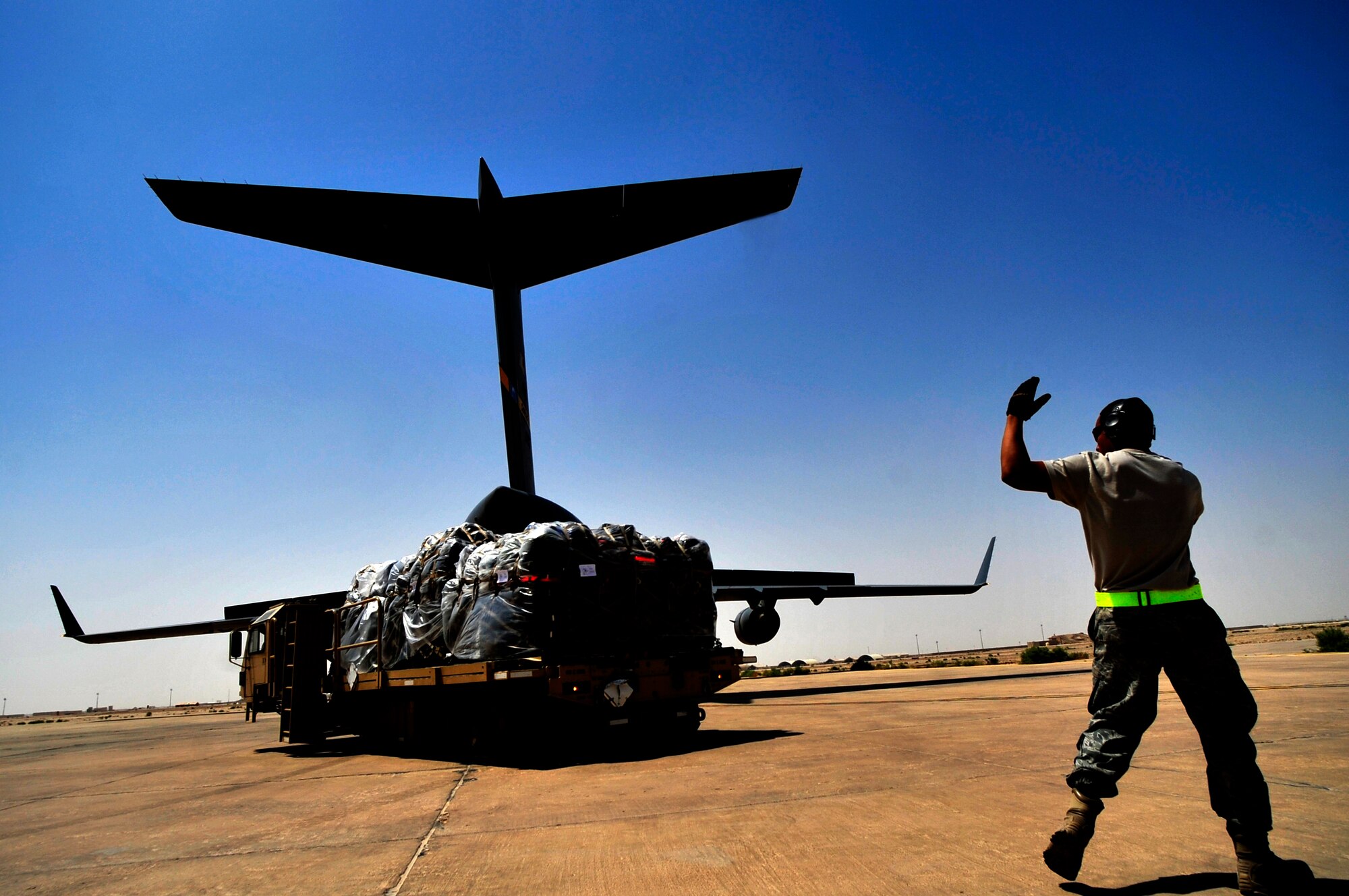 An aerial porter marshals a K-Loader vehicle with cargo from a C-17 Globemaster III transport aircraft at Ail Base, Iraq on Aug. 26, 2011.  The terminal is the southern aerial hub of Iraq.  It processes approximately 5,000 passengers and 850,000 pounds of cargo each month. (U.S. Air Force photo/Master Sgt. Cecilio Ricardo) 