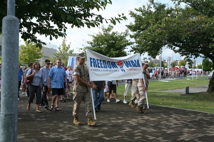 Cpl. Jose Casal, consolidated automatic support system technician, and Lance Cpl. Brittany Daniels, administrative specialist, both with Marine Aircraft Logistics Squadron 12, hold the banner and lead approximately 275 station residents to the Marine Memorial Chapel here Sunday during the 6th annual Freedom Walk September 11, 2001, remembrance ceremony.