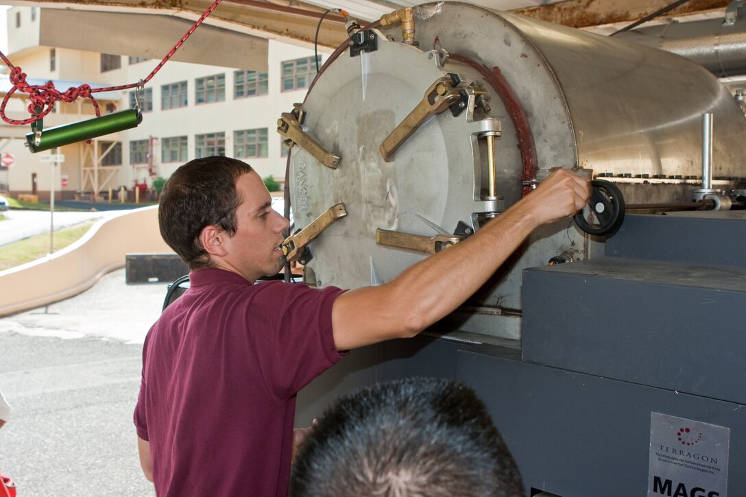 CAMP H. M. SMITH, HI - Leon Labry, the MAGS manufacturer's representative, demonstrates the loading process of the Micro Auto Gasification System (MAGS) waste disposal process to chemistry students from Damien Memorial High School Sept. 12.  The MAGS is a prototype being tested by MARFORPAC which reduces solid waste by as much as 95 percent while dramatically reducing carbon dioxide emissions.  The demonstration was part of the MARFORPAC Commander's Science, Technology, Engineering and Math (STEM) support program to local high schools. (USMC photo by Chuck Little)