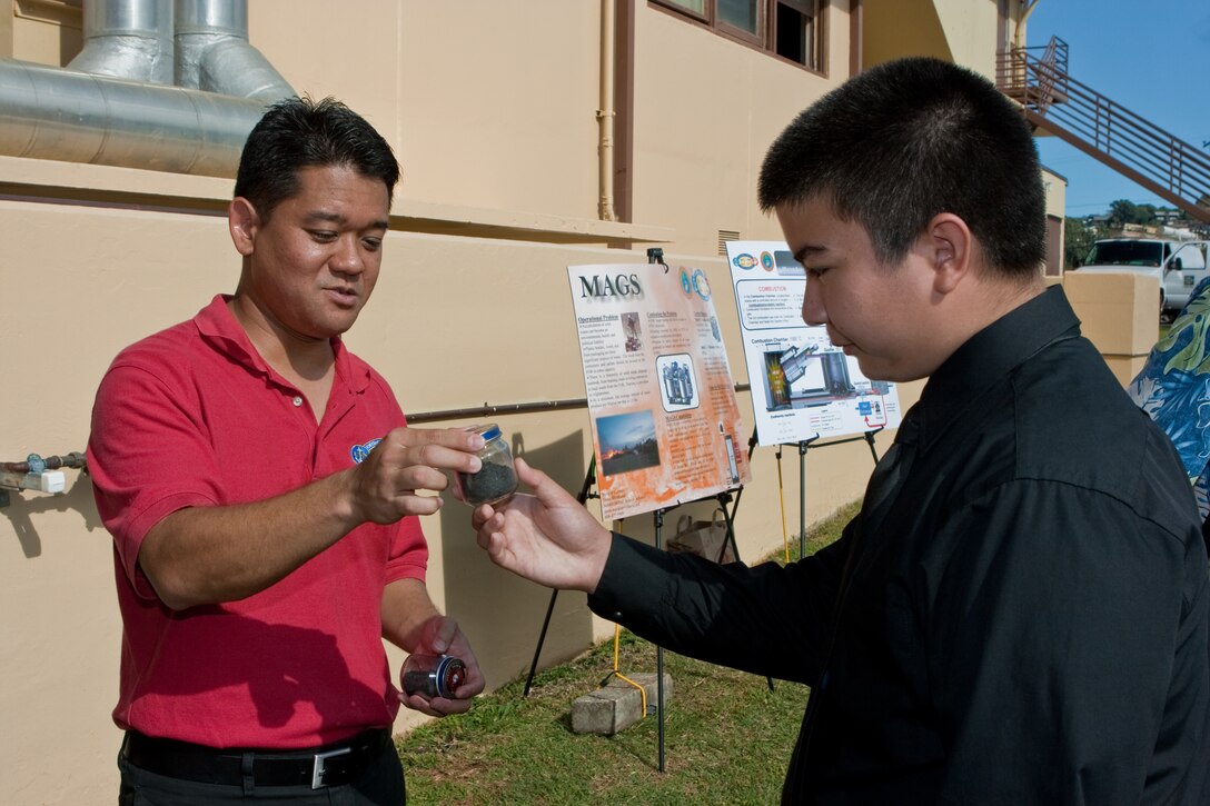 CAMP H. M. SMITH, HI - Donn Murakami, the U.S. Marine Corps Forces, Pacific Science Advisor, hands Damien Memorial High School junior chemistry student Brian Lab a small jar containing the waste residue produced by processing a large bag of garbage through the Micro Auto Gasification System (MAGS) Sept. 12.  The MAGS is a prototype being tested by MARFORPAC which reduces solid waste by as much as 95 percent while dramatically reducing carbon dioxide emissions.  The demonstration was part of the MARFORPAC Commander's Science, Technology, Engineering and Math (STEM) support program to local high schools. (USMC photo by Chuck Little)