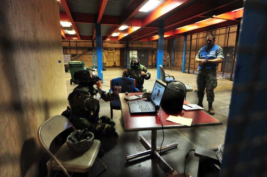Airmen from the 22nd Air Refueling Wing “command post” don their gas masks as exercise evaluation team member Master Sgt. Ronald Flack, 22nd ARW Public Affairs NCO in charge of visual information, observes Sept. 11, 2011 at McConnell Air Force Base, Kan. Approximately 300 team McConnell Airmen participated in a two day exercise. (U.S. Air Force photo by Senior Airman Courtney Witt)
