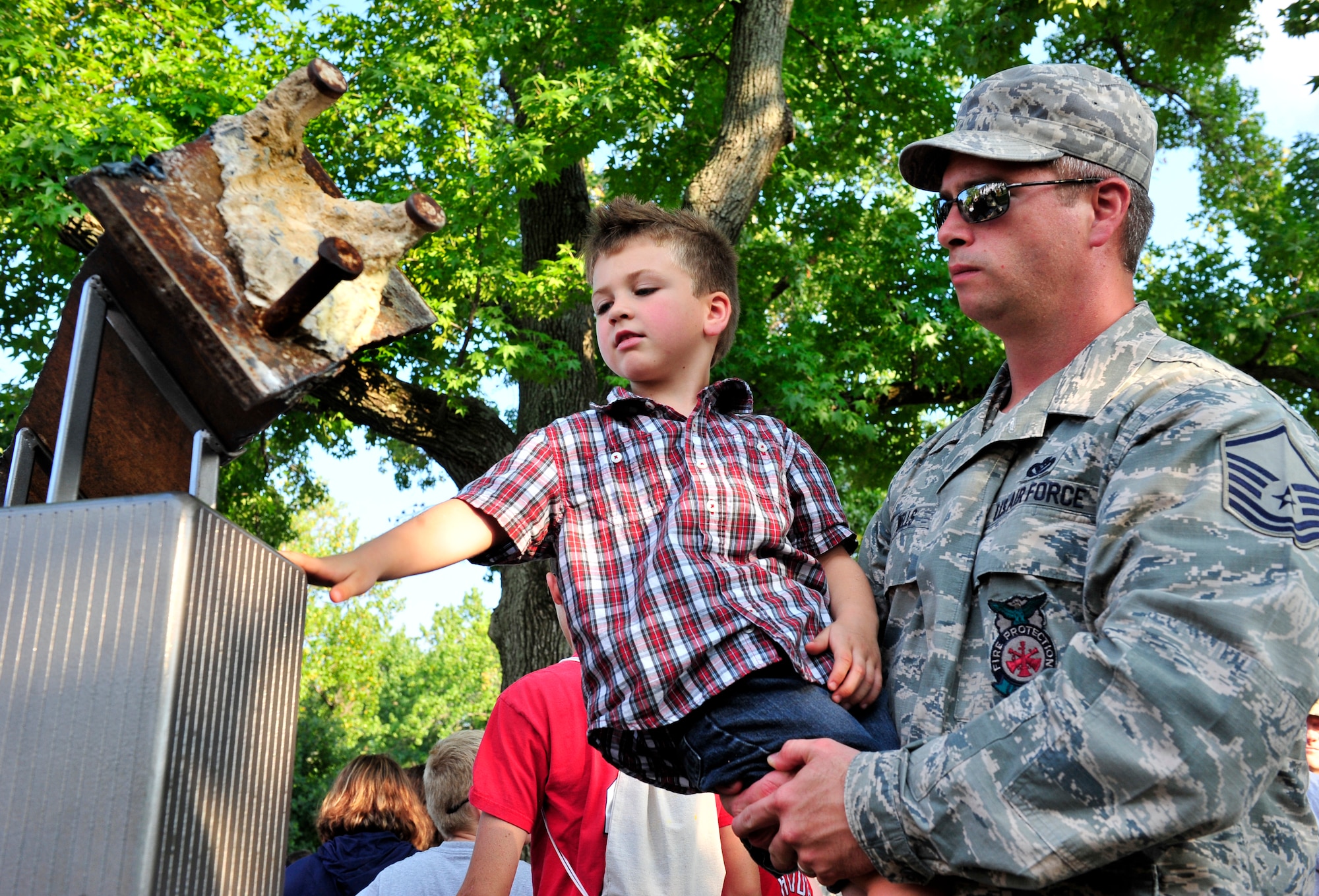 Master Sgt. Brian Wells, 375th Civil Engineer Squadron fire protection, and his son Brennon, 5, touch the 9/11 monument during the observance ceremony on Scott Air Force Base, Ill.  The Scott monument is made of four pieces: a pentagon shaped-planter constructed of Indiana limestone--the same material used in the façade of the Pentagon. Within the planter, new foliage representing life is planted in soil from Pennsylvania; Twin Tower replicas emerge from the center, made of brushed steel in the same style as the fallen towers. And a steel beam from the Twin Towers. The monument now offers a place of reflection for families, military members and civilian guests. (U.S. Air Force photo, Staff Sgt. Stephenie Wade)