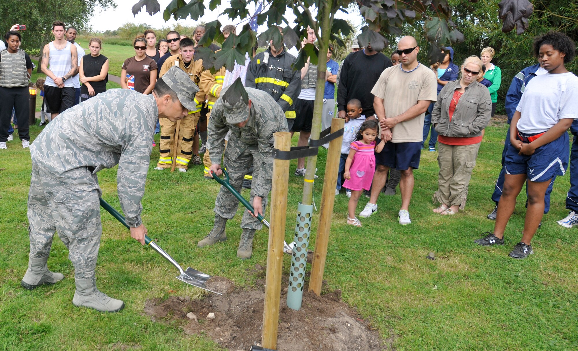 ROYAL AIR FORCE LAKENHEATH, England - Col. John Quintas, 48th Fighter Wing commander, and Chief Master Sgt. John Mazza, 48th Mission Support Group command chief, shovel dirt during a tree dedication ceremony as Airmen and families look on to honor victims of 9/11 at Peacekeeper Park, Sept. 11, 2011. The tree dedication followed a 24-hour run that ended at 1:46 p.m. on Sept. 11, 2011, the time the first tower was hit. (U.S. Air Force photo by Senior Airman Tiffany M. Deuel)