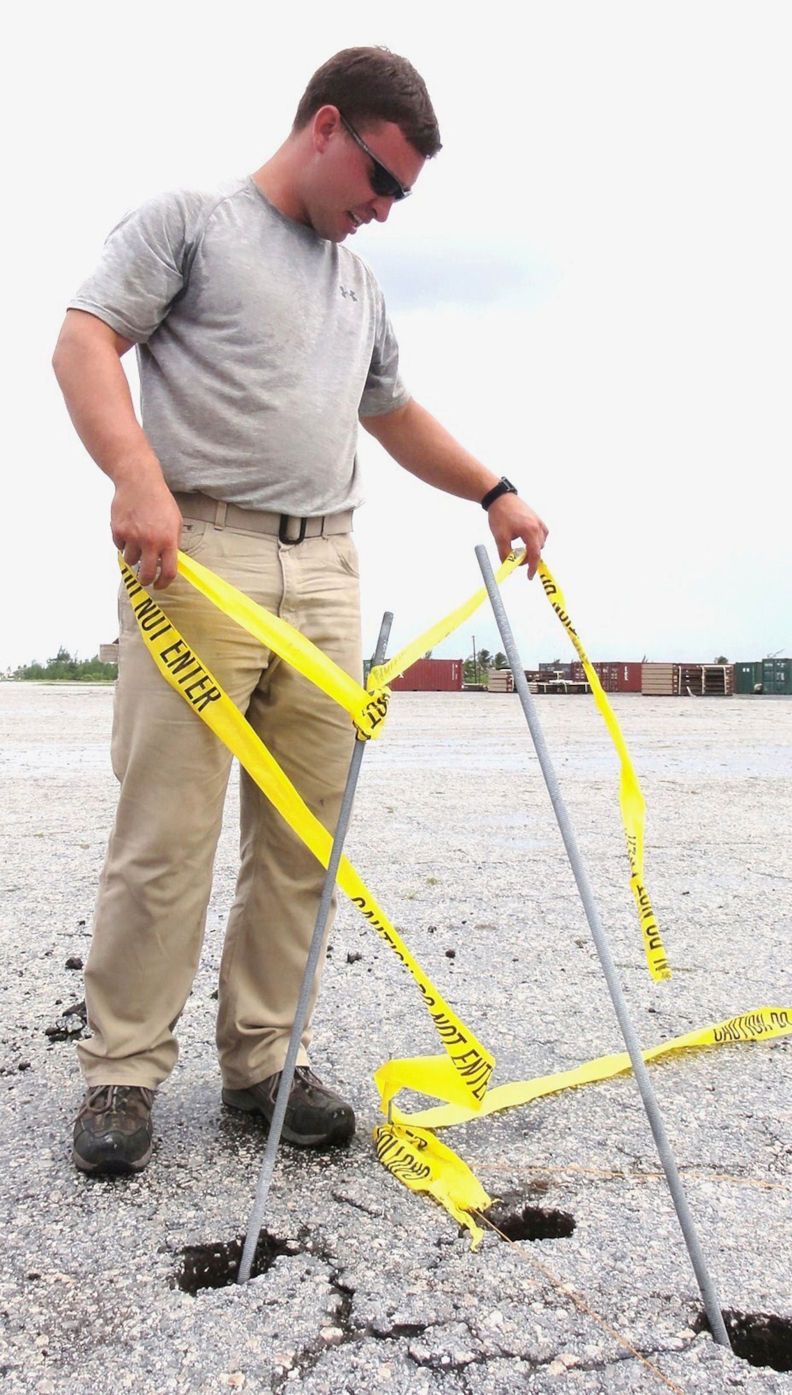 Staff Sgt. Andrew Worrick, 611th CES electrician, adjusts caution tape on an anchor for a Sprung structure.  A three-man crew from the 611th formed the advance team to install the anchors before the rest of the 7-man team arrived.  The advance team installed about 26 pairs of manta-ray anchors in the pavement to keep the frame of the Sprung structure secure. (Photo by U.S. Air Force Capt. Amy Hansen)   