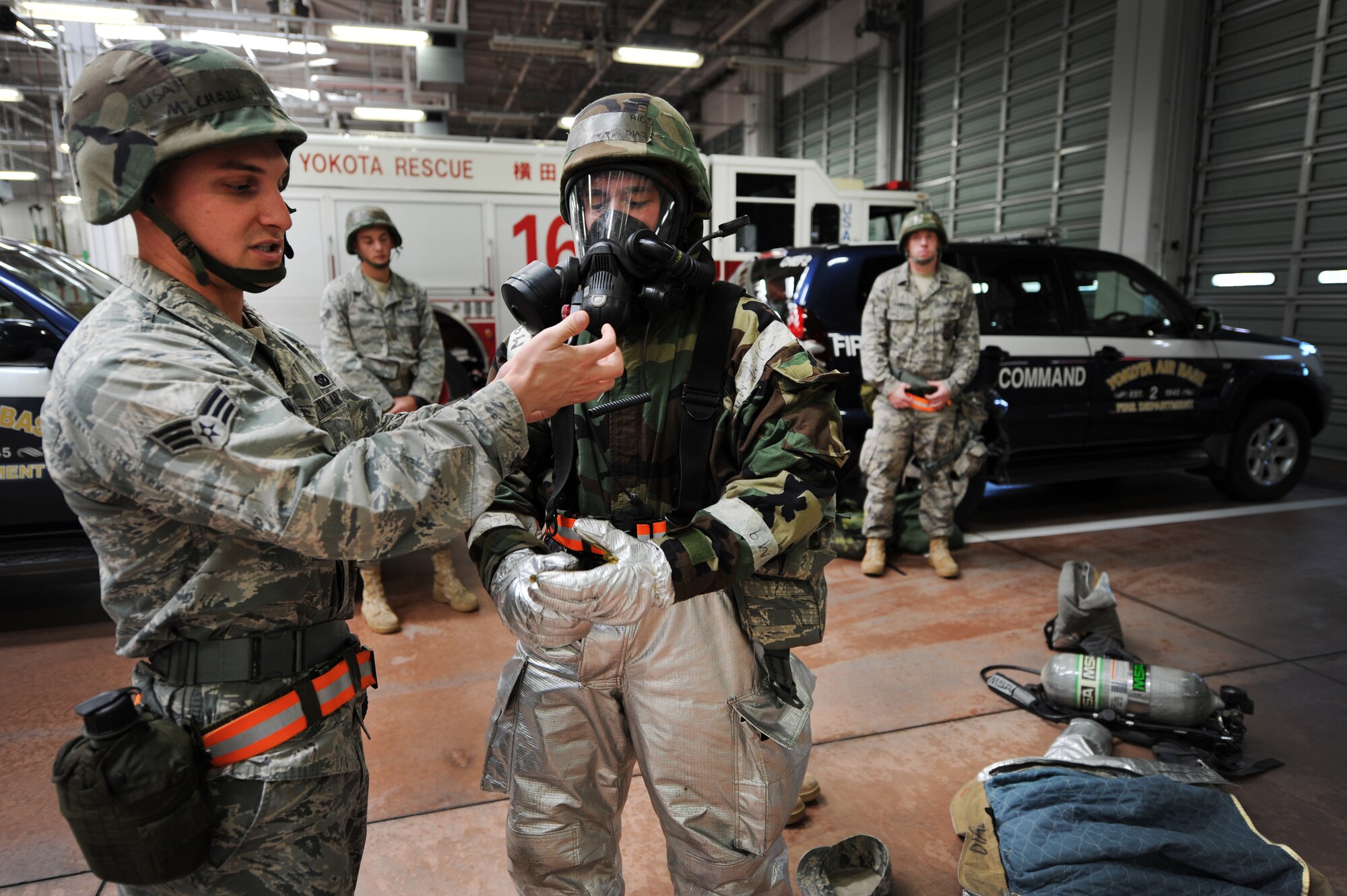 YOKOTA AIR BASE, Japan – Senior Airman Michael Waffle and Airman 1st Class Christopher Diaz, firefighters in the 374th Civil Engineer Squadron, demonstrate how to wear the additional gear required for firefighters to respond in a chemical environment at Yokota Air Base, Japan, Sept. 13, 2011. Yokota recently participated in an operational readiness exercise. (U.S. Air Force photo/Staff Sgt. Stacy Moless)