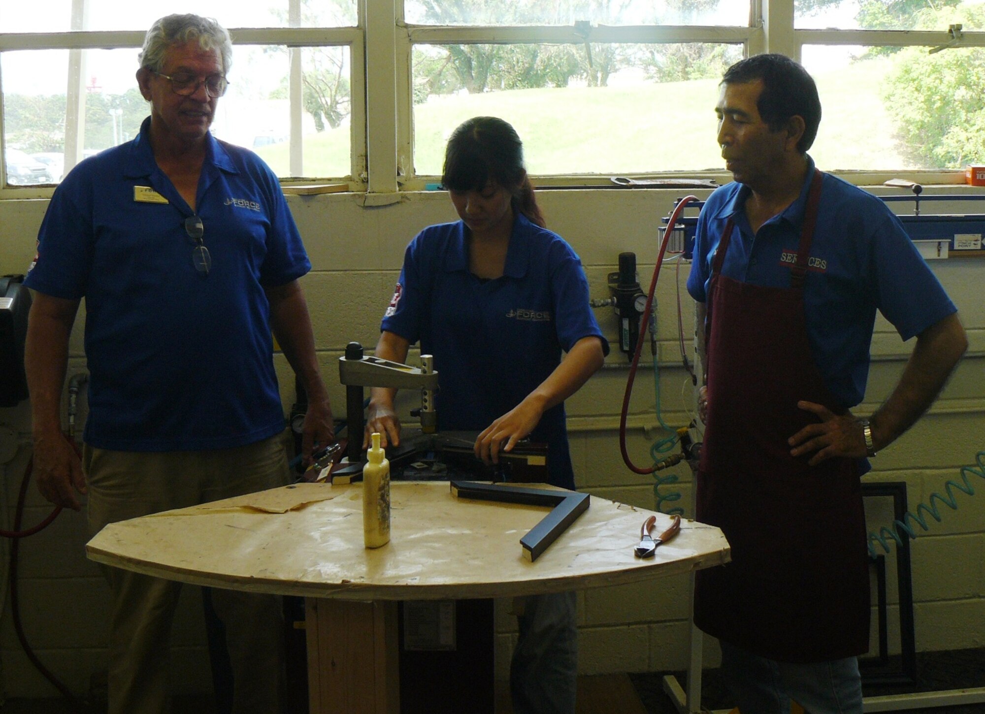 Mako Matsumoto, Kadena Language Institute intern (center), makes a frame at the arts and crafts center on Kadena Air Base, Japan, while Michael Westfall and Hideaki Iha from the center observe during the August to September KLI internship here. The internship program, instituted more than 12 years ago, is aimed at helping the second-year students of KLI gain confidence and proficiency in their English-speaking skills. (Courtesy photo/Kadena Language Institute)