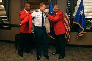 T.J. Spann, Tidewater Chapter-Tuskegee Airmen Incorporated president, and Grant Williams Sr, Tidewater Chapter-Tuskegee Airmen Incorporated speakers bureau chairman, help U.S. Air Force Gen. William M. Fraser III, commander of Air Combat Command, put on his red jacket during the Honorary Tuskegee Airmen event at Langley Air Force Base, Va., Sept. 8, 2011. The jacket is a historical nod to the Red Tail P-51 flown by the Tuskegee Airmen, who were supported by nearly 19,000 Tuskegee Airmen ground-support forces.  (U.S. Air Force photo by Airman 1st Class Racheal Watson/Released)