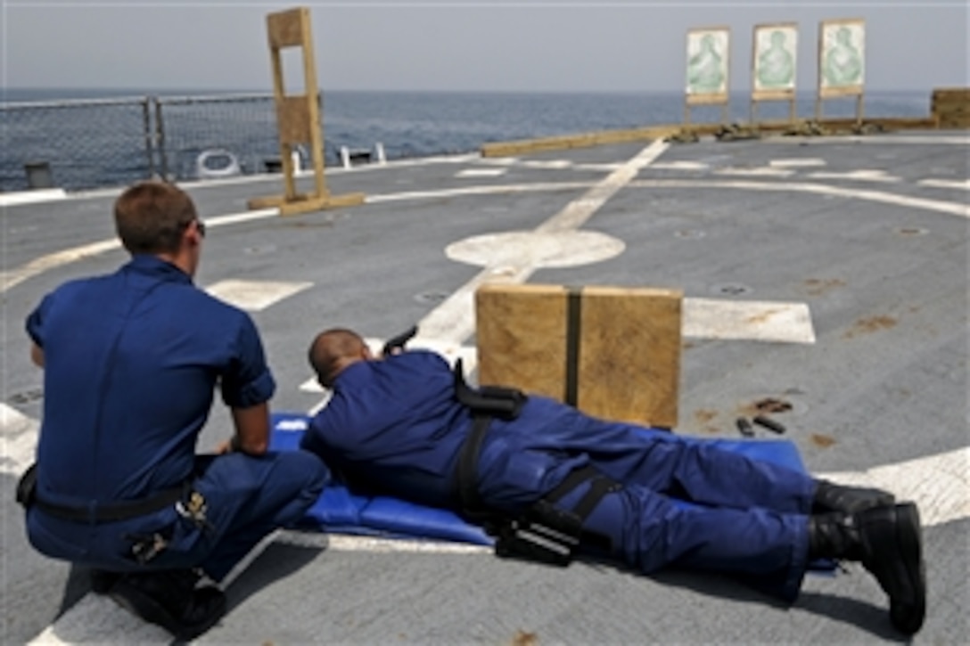 U.S. Navy Petty Officer 2nd Class Travis Kaizen watches as Petty Officer 1st Class Kenny Carriel fires a 9mm pistol during weapons qualification aboard the guided-missile destroyer USS Mitscher in the Gulf of Aden, Sept. 5, 2011. Kaizen is a gunner's mate and Carriel is an interior communications electrician.