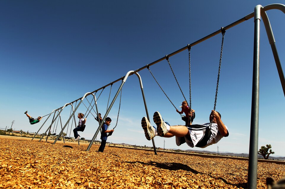 Cpl. Joseph Bishop [right], an ammunition chief and volunteer from Headquarters Battalion, shows the children of Joshua Tree Elementary School the finer points of swinging at the school's playground Sept. 14, 2011. The Marines were there as part of the Adopt-a-School program where the unit could interact with schools in the local community.